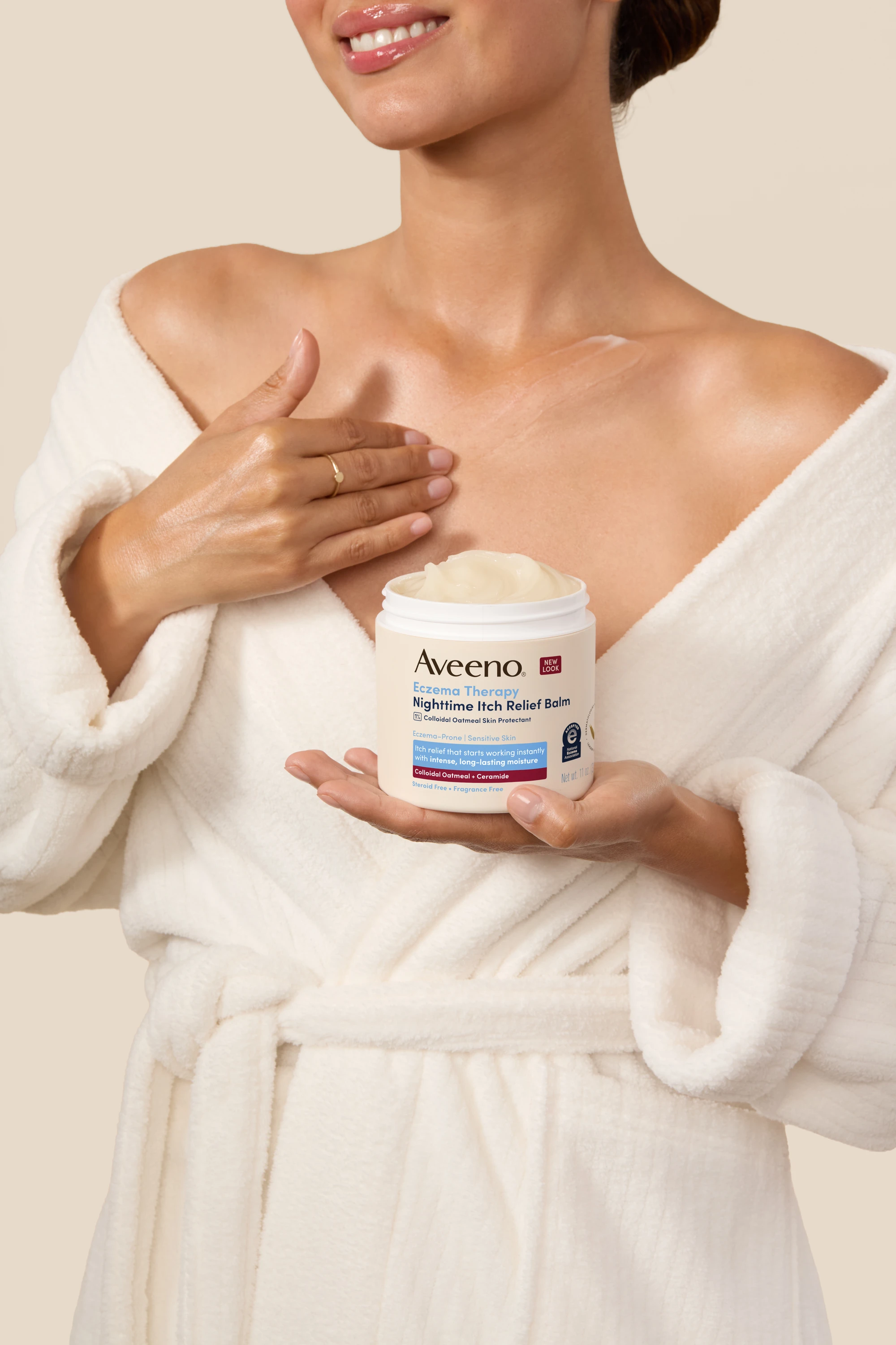 A model in a robe holding an Aveeno jar.