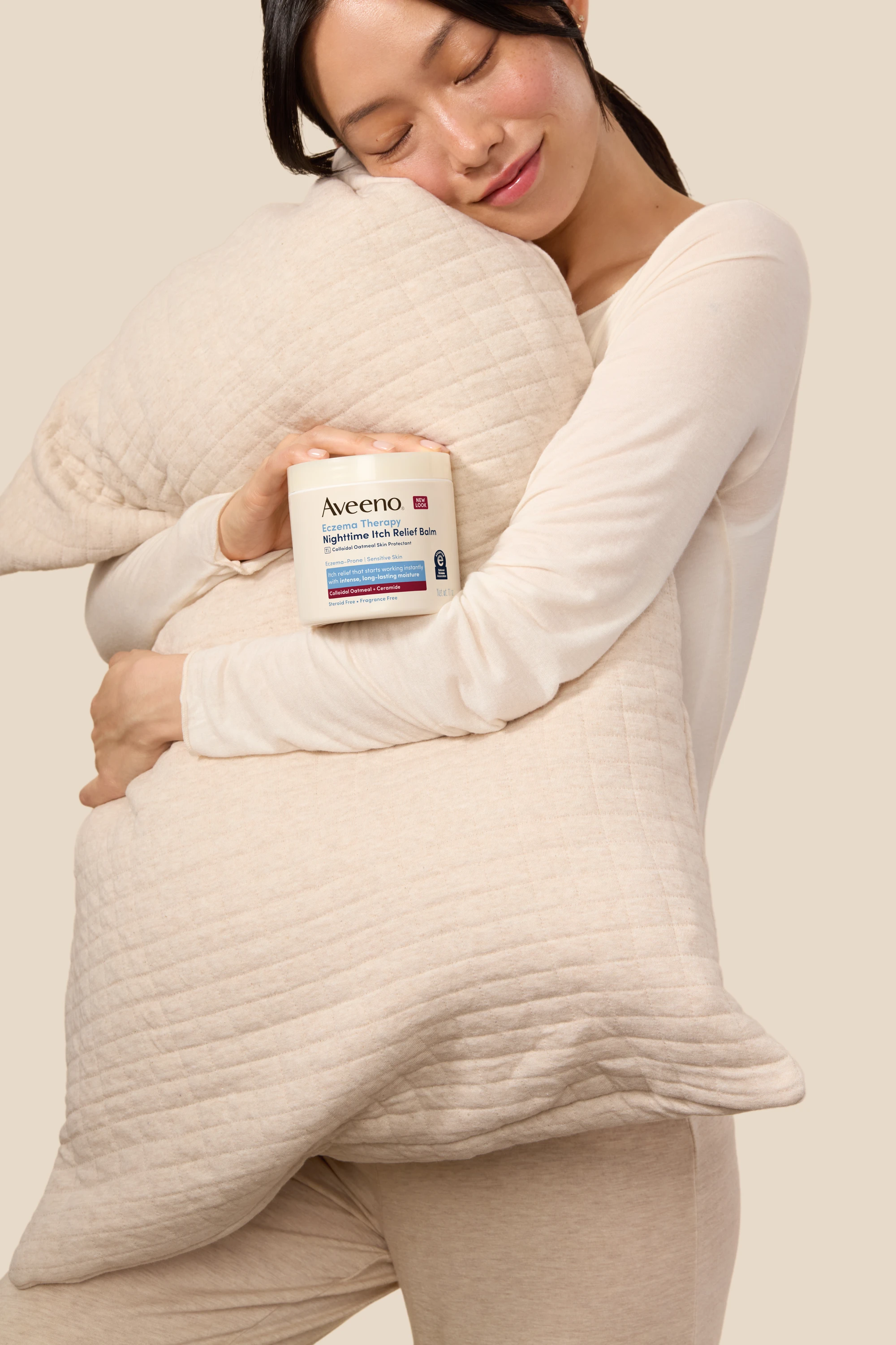 A model hugging a pillow while holding an Aveeno jar.