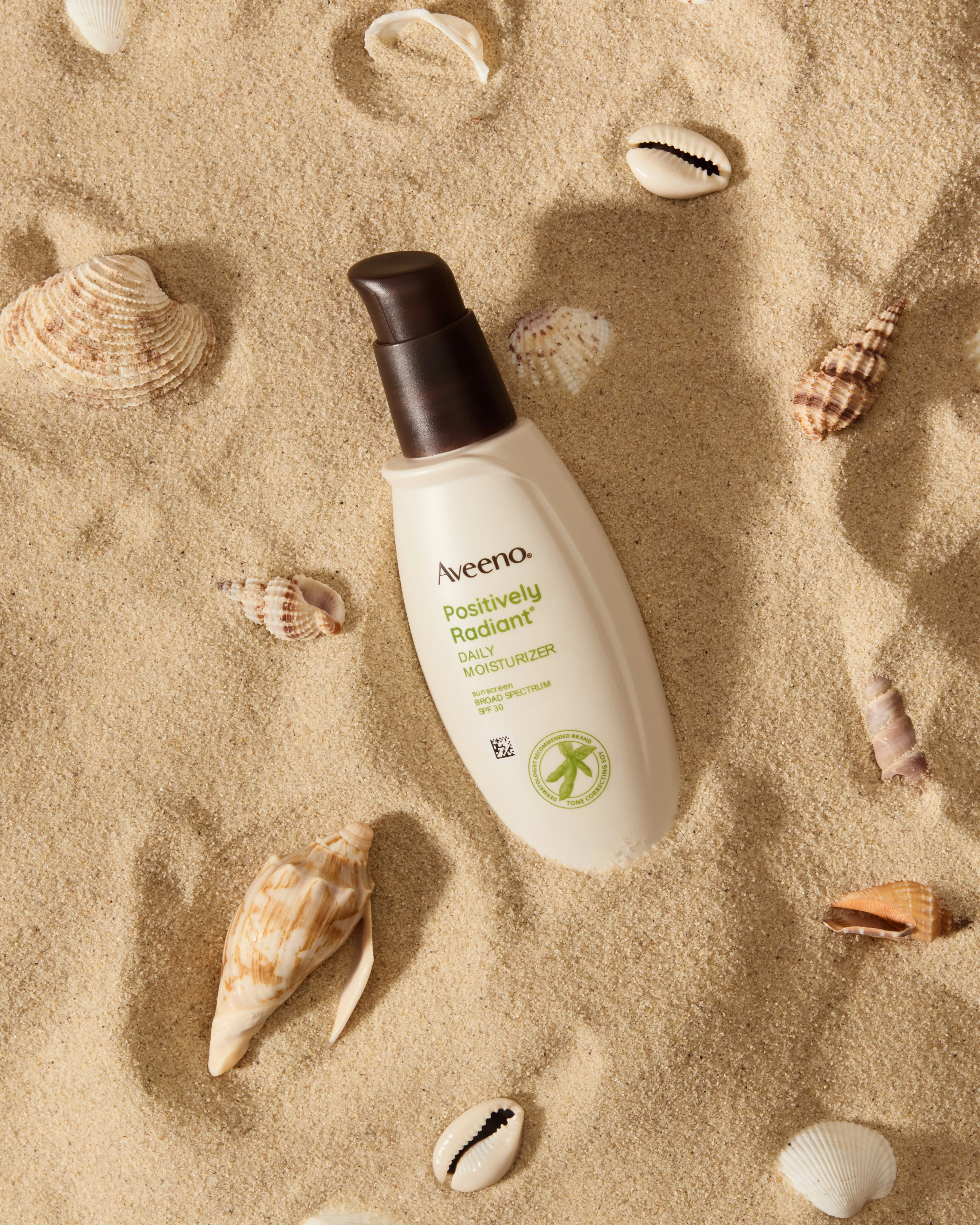 An Aveeno spray bottle on sand surrounded by shells.