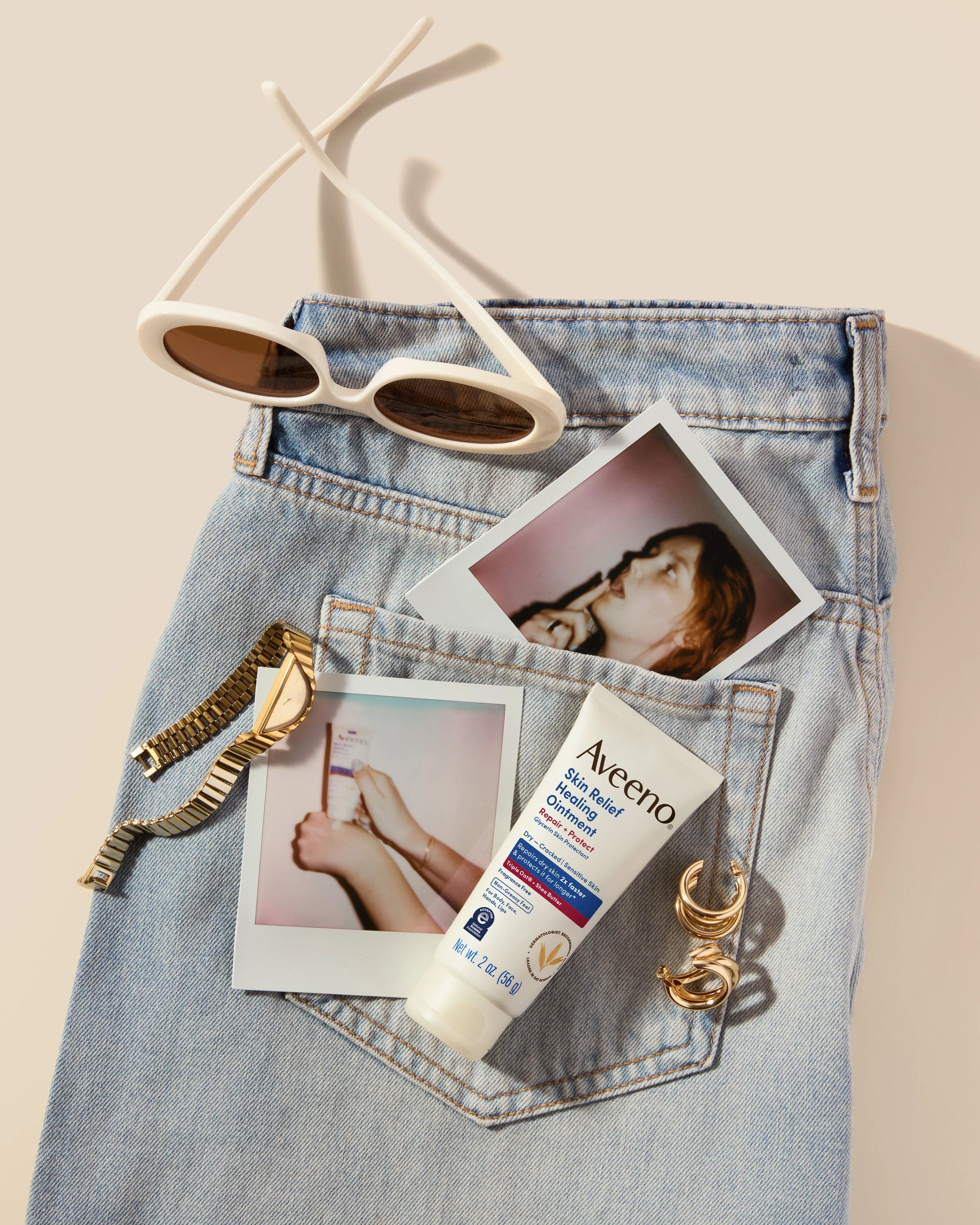 An Aveeno tube tucked into a jeans pocket with photographs and sunglasses.