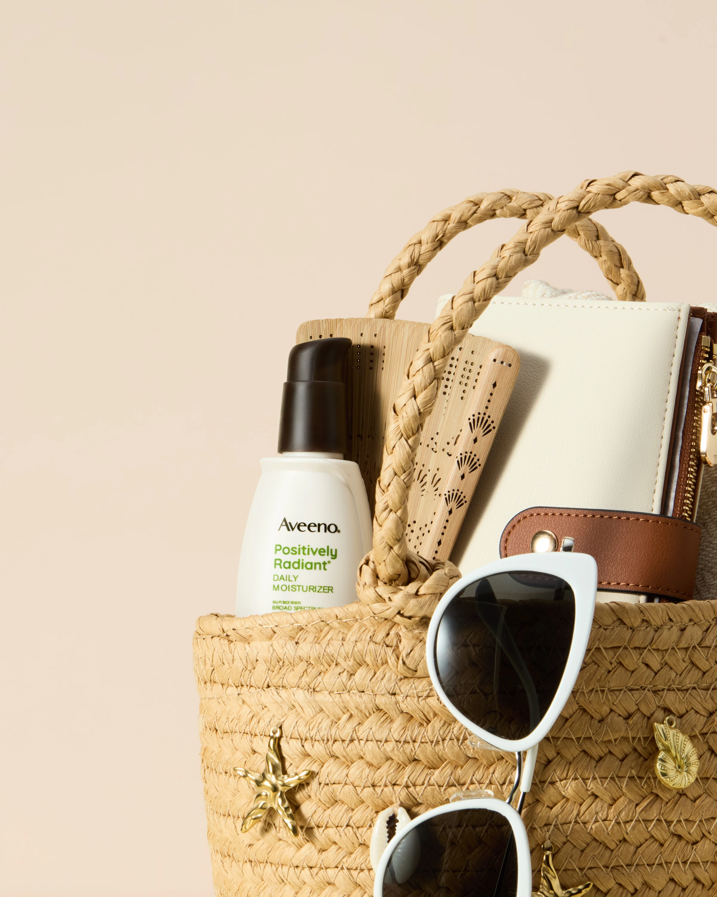 An Aveeno spray bottle and accessories in a woven beach bag.