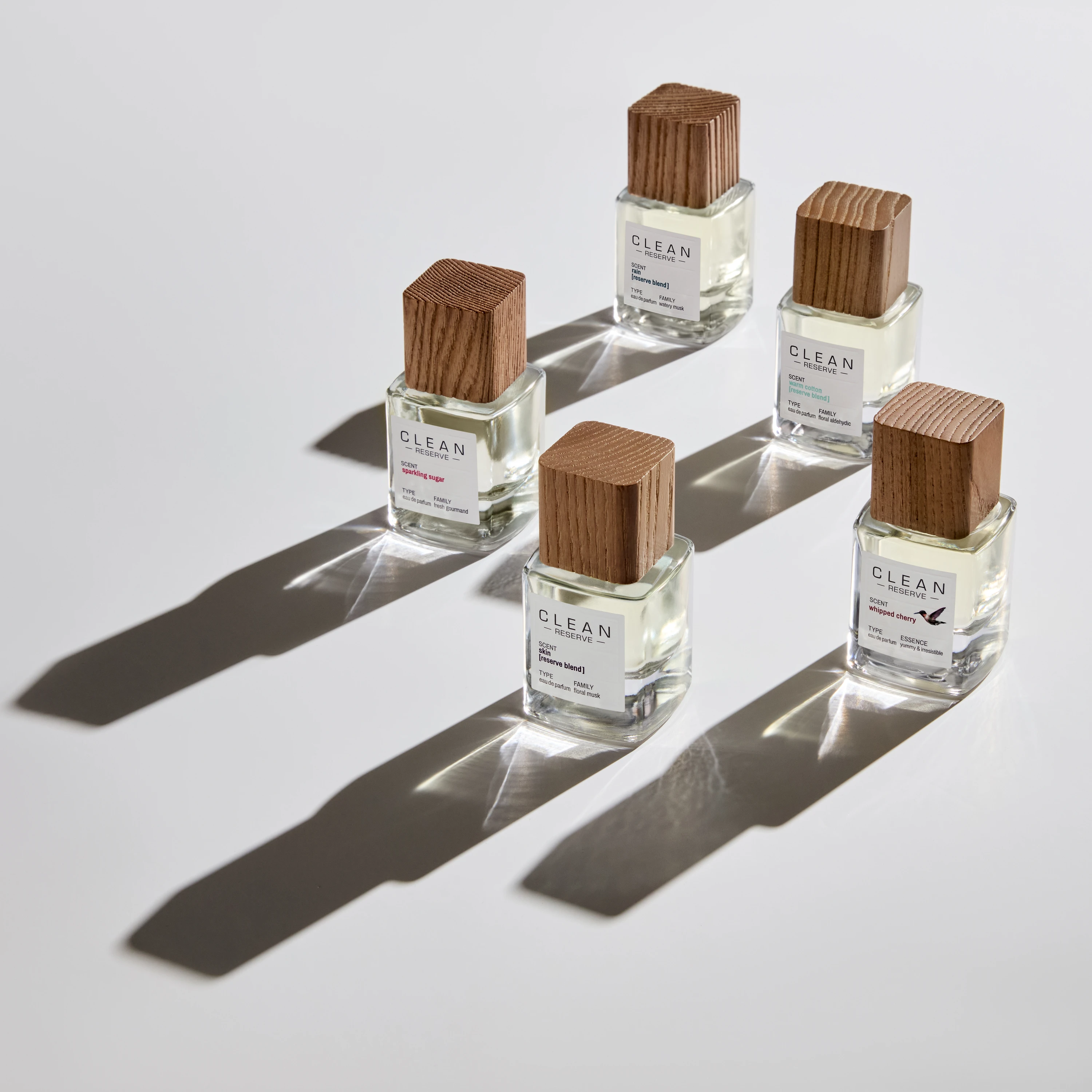 Five Clean Reserve fragrance bottles casting long shadows.