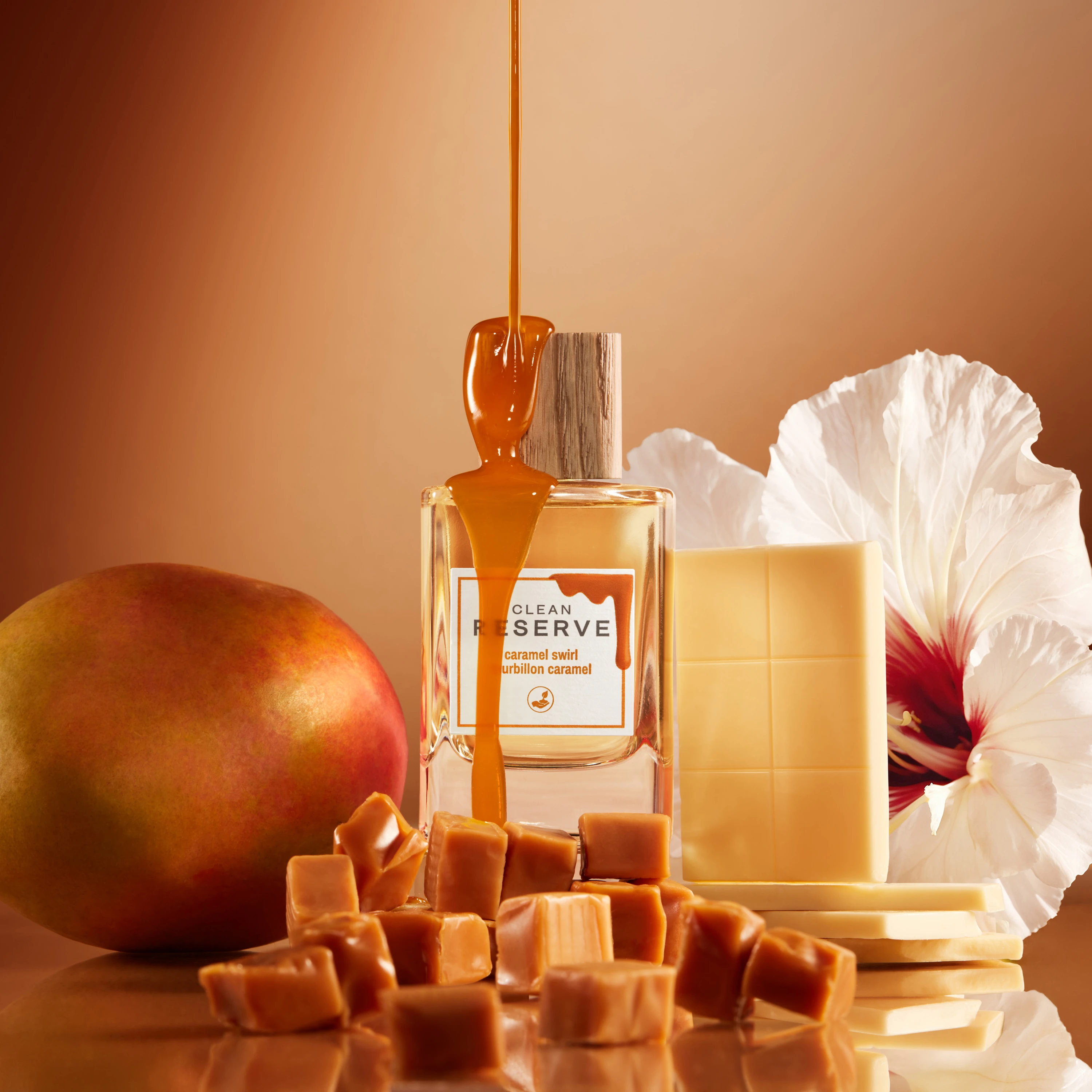 A Clean Reserve bottle and cap surrounded by orange-toned ingredients.