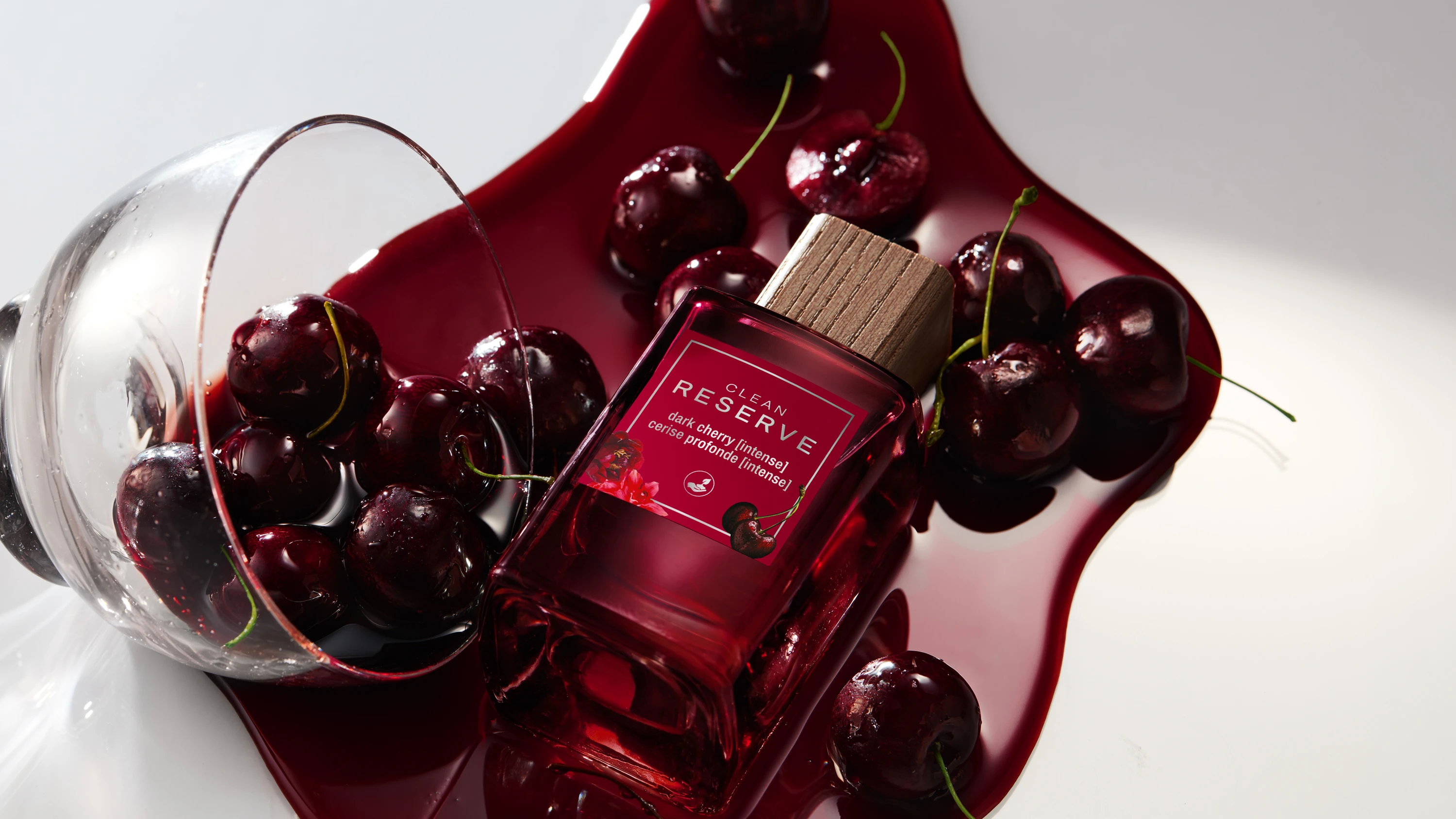 A dark red Clean Reserve bottle inside a tipped glass with cherries.