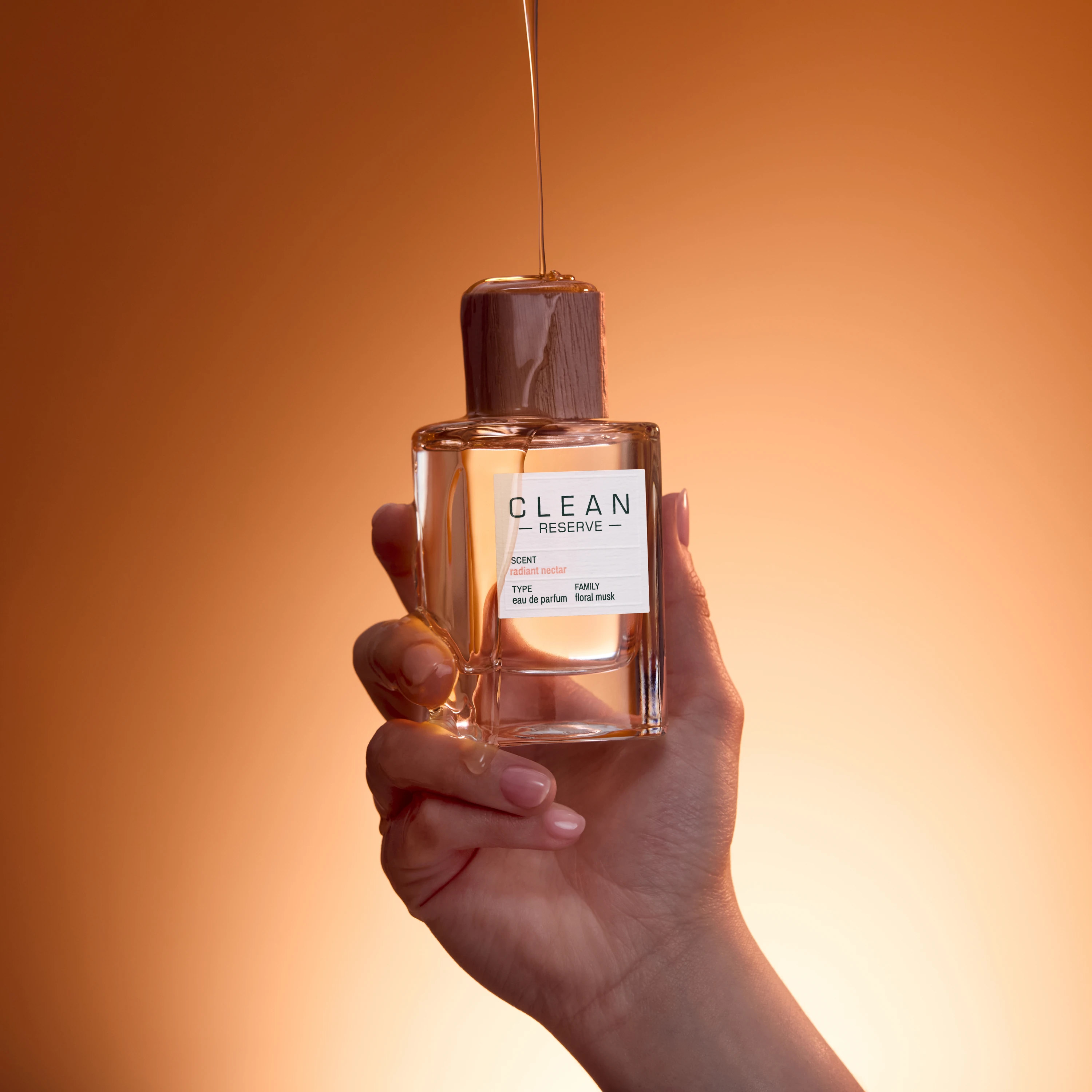A hand holding a Clean Reserve bottle against an orange background.