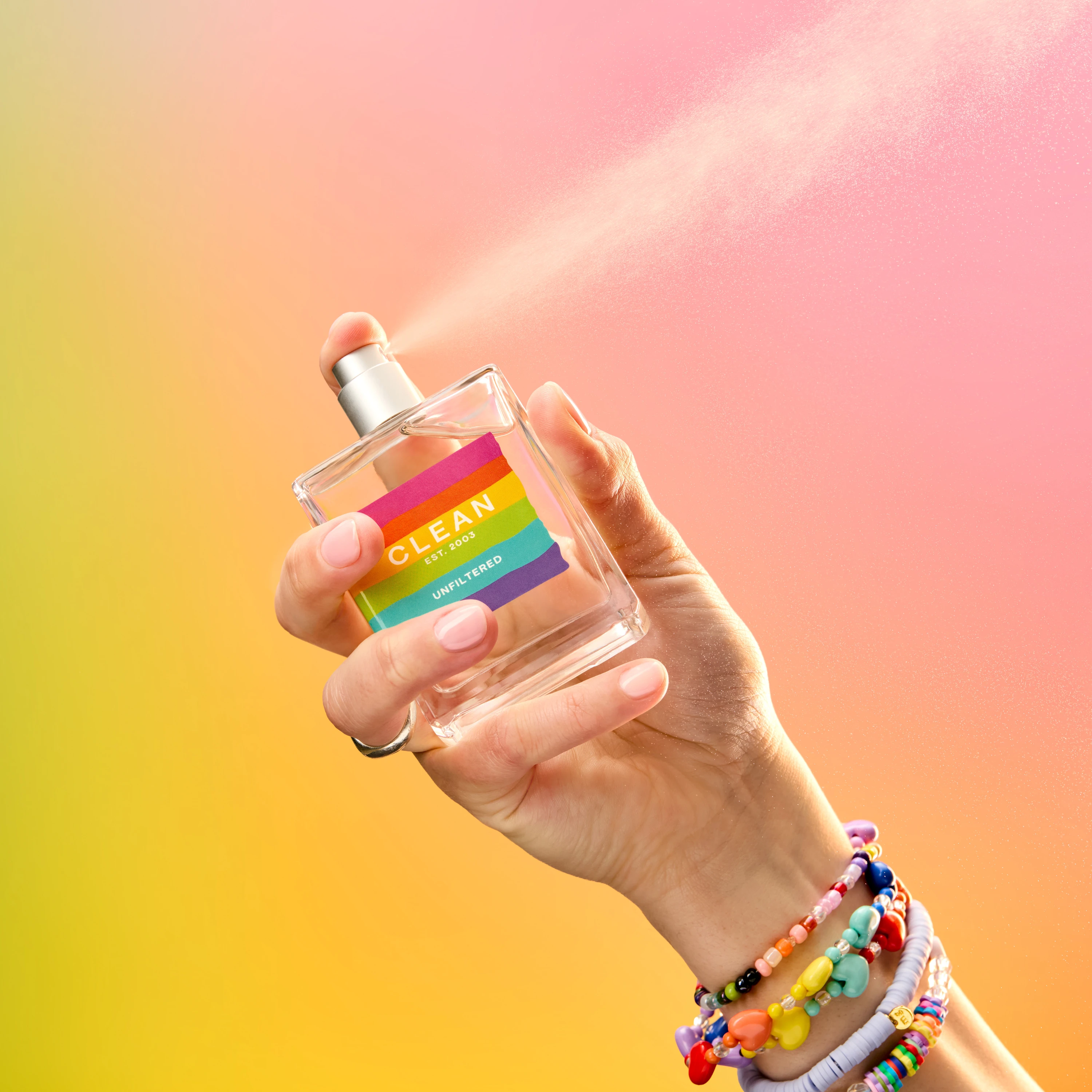 A hand holding a Clean fragrance bottle with colorful bracelets.