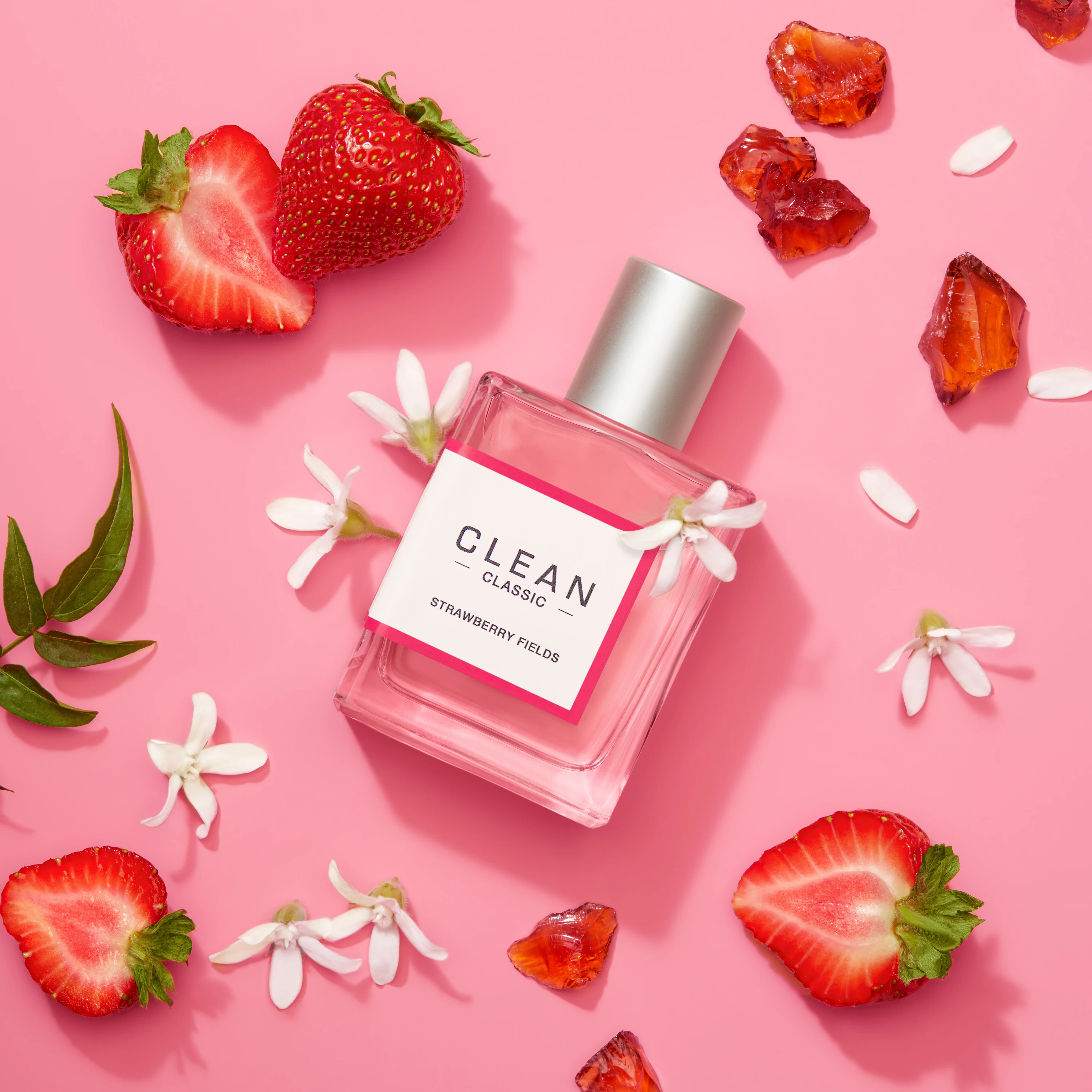 A pink Clean fragrance bottle surrounded by strawberries and flowers.