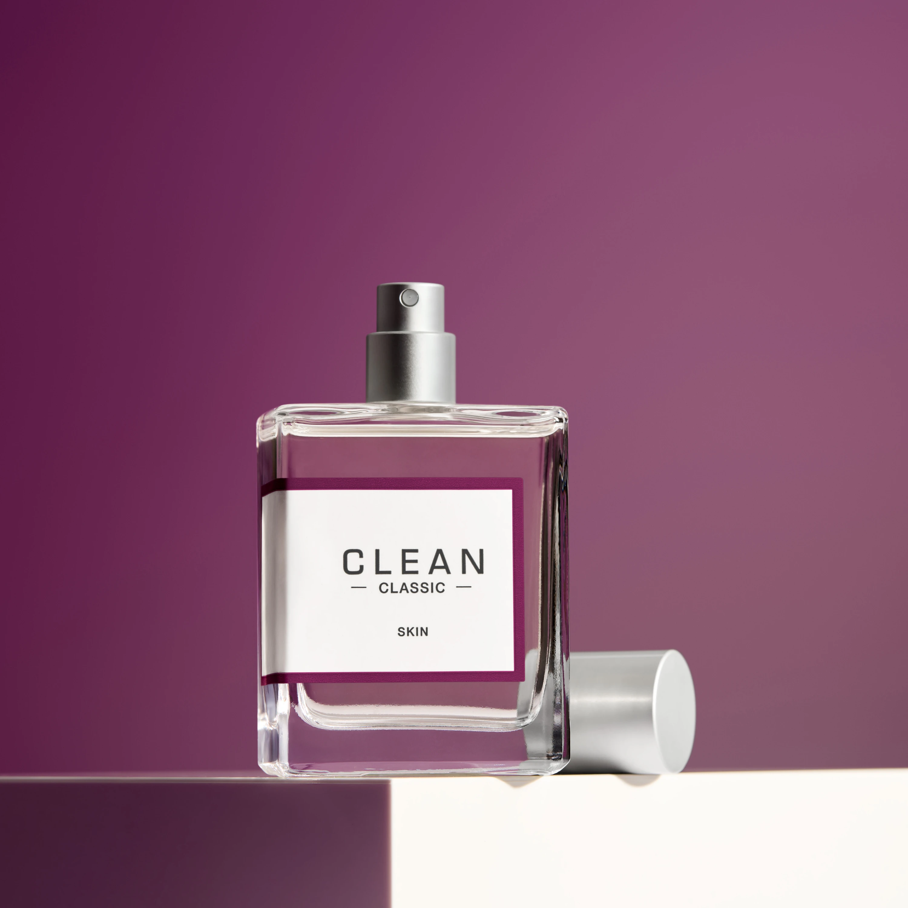 A Clean fragrance bottle and cap against a plum background.