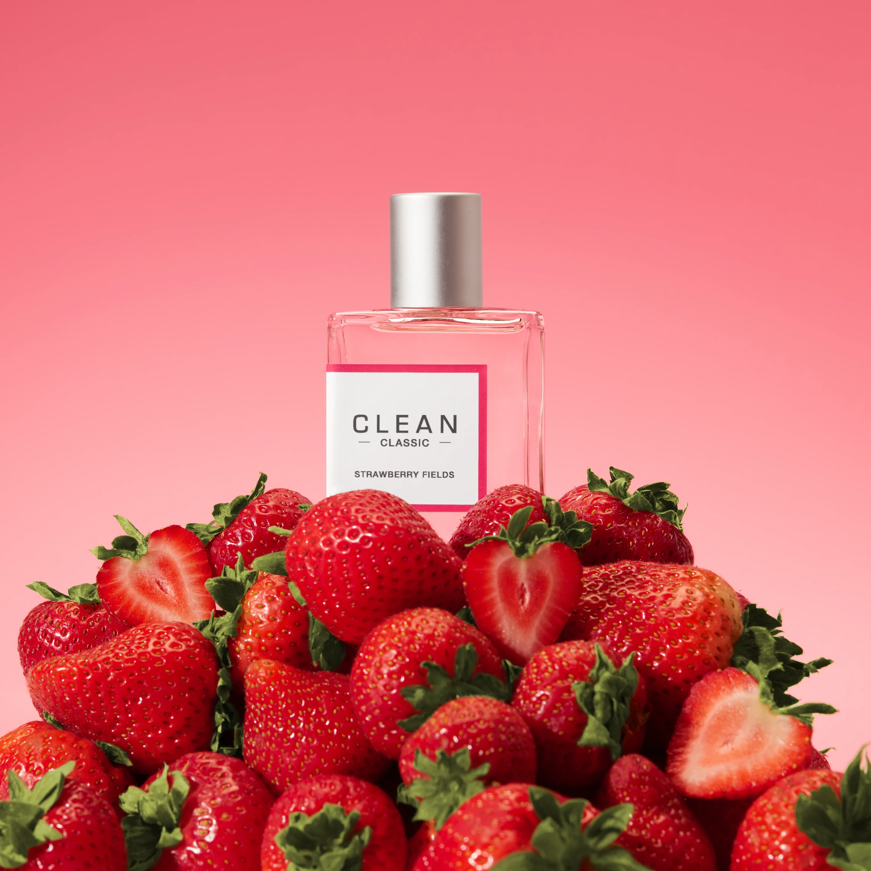 A pink Clean fragrance bottle resting among strawberries.