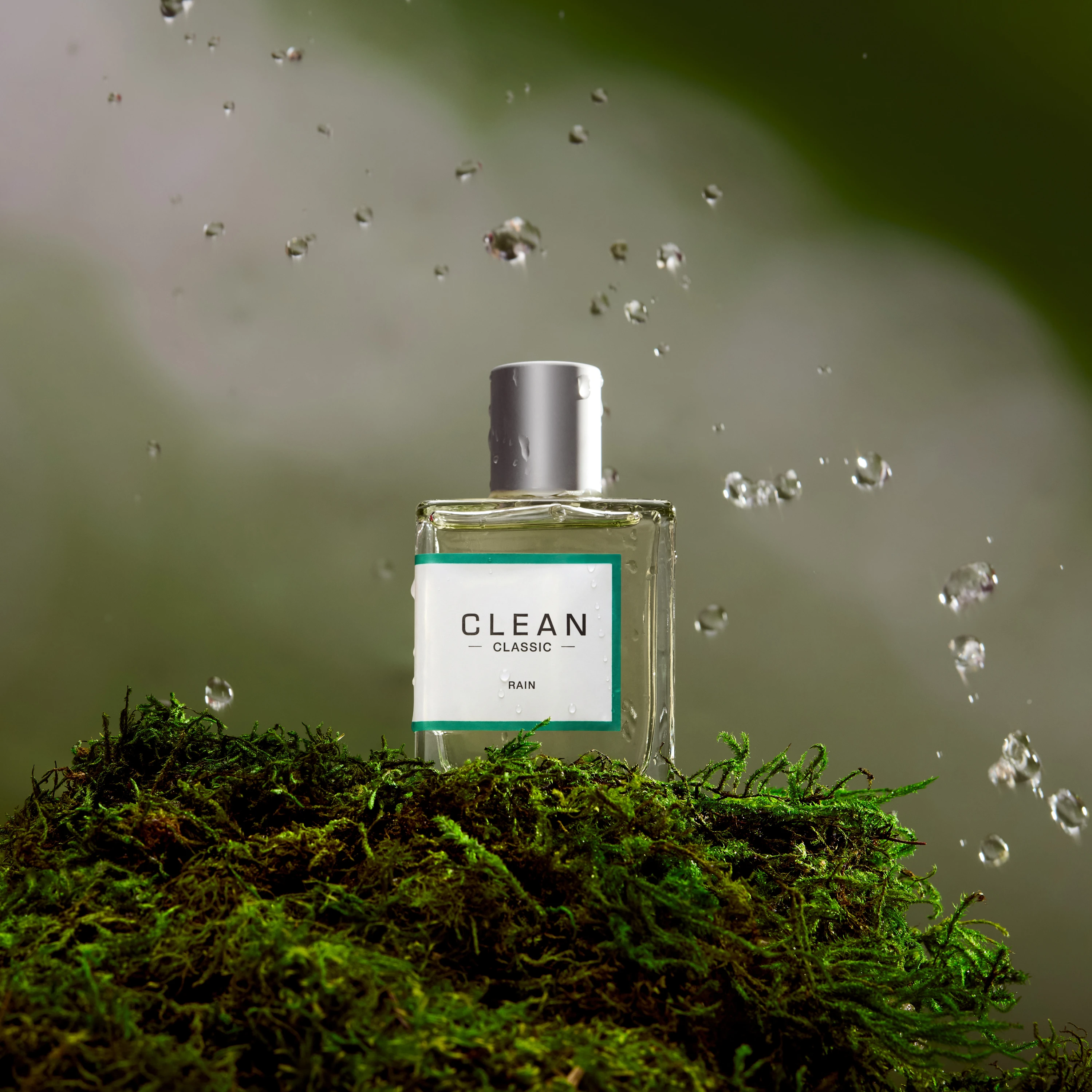 A Clean fragrance bottle on moss with airborne droplets.
