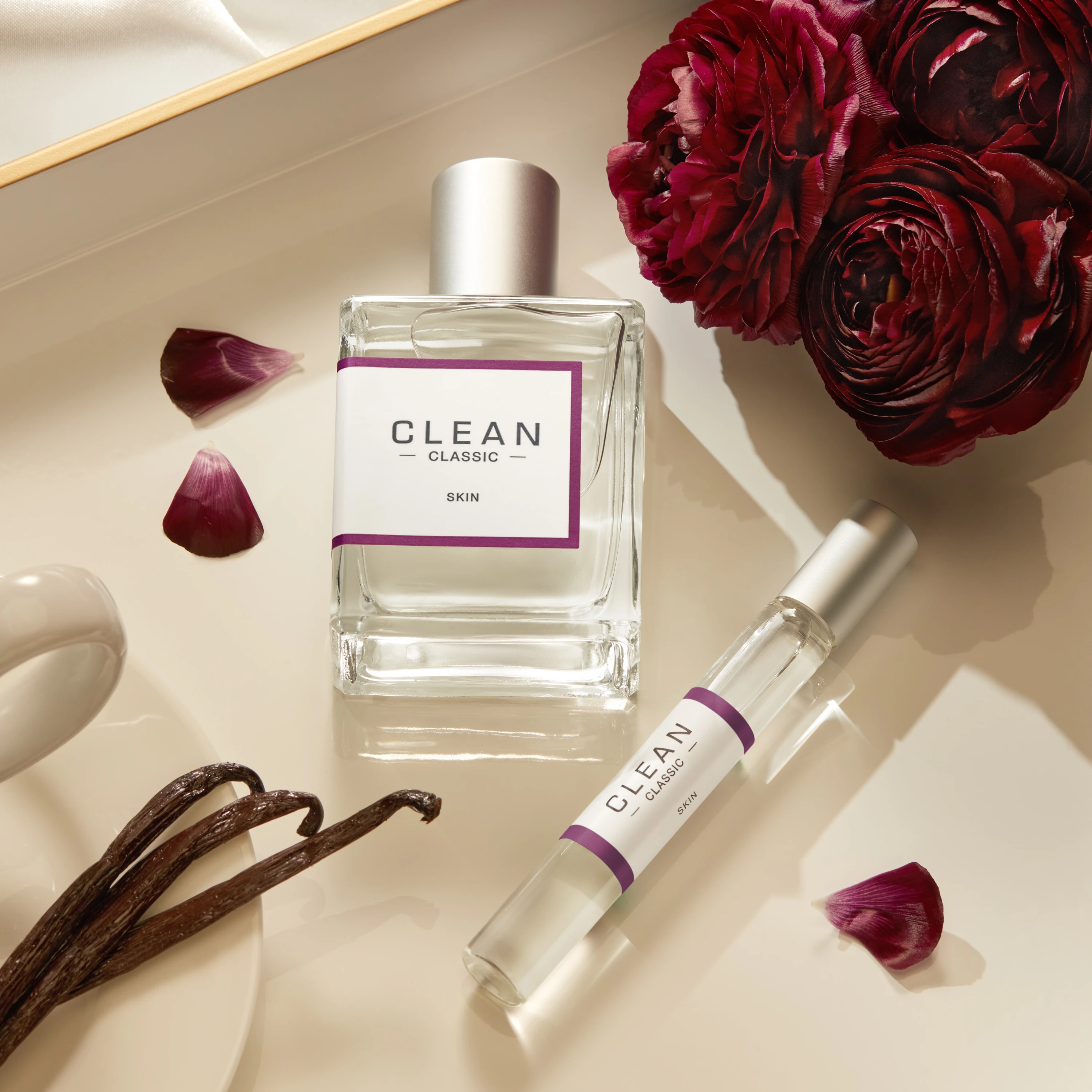 Clean fragrance bottle and travel spray beside red flowers and vanilla pods.