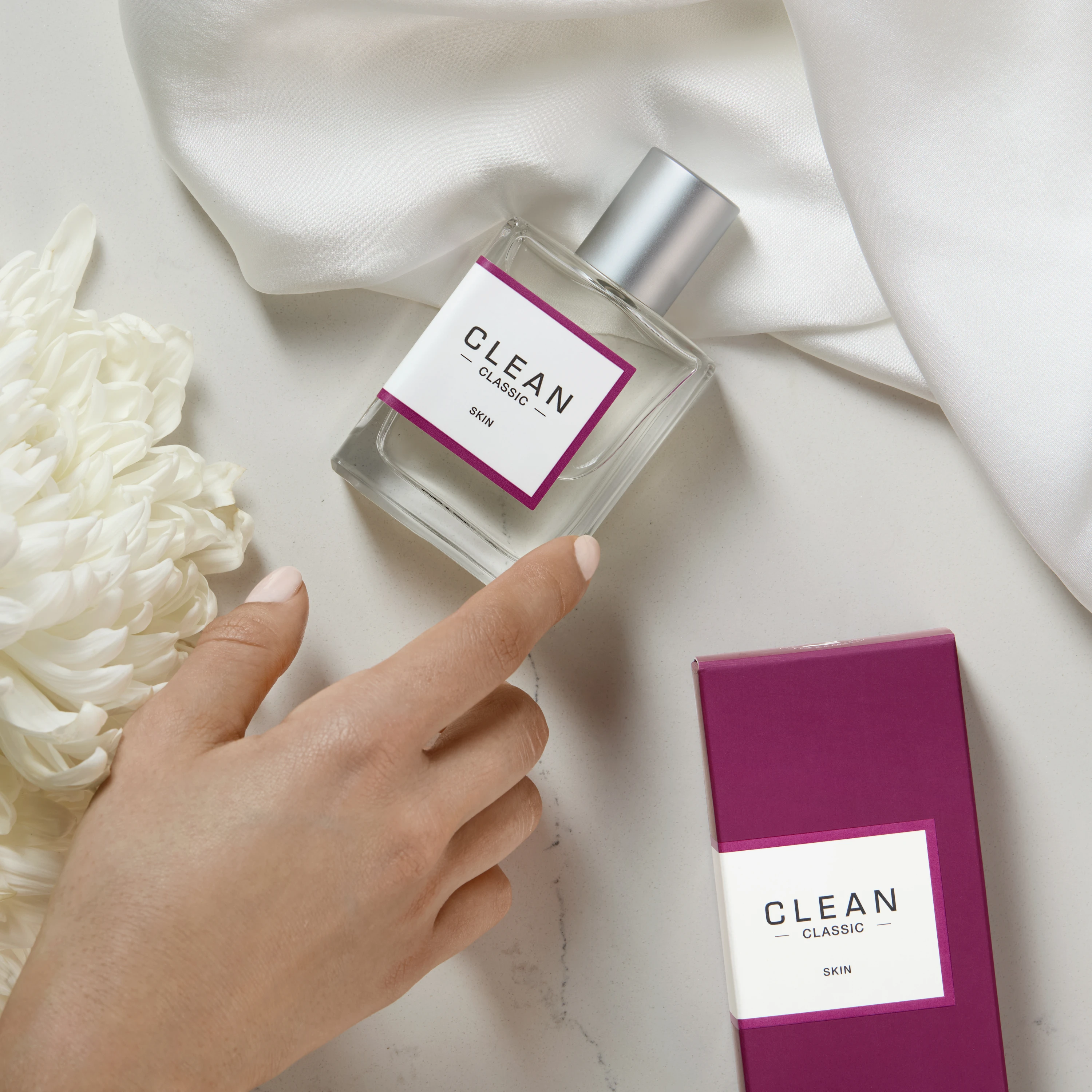 A hand reaching toward a Clean fragrance bottle on pale fabric.