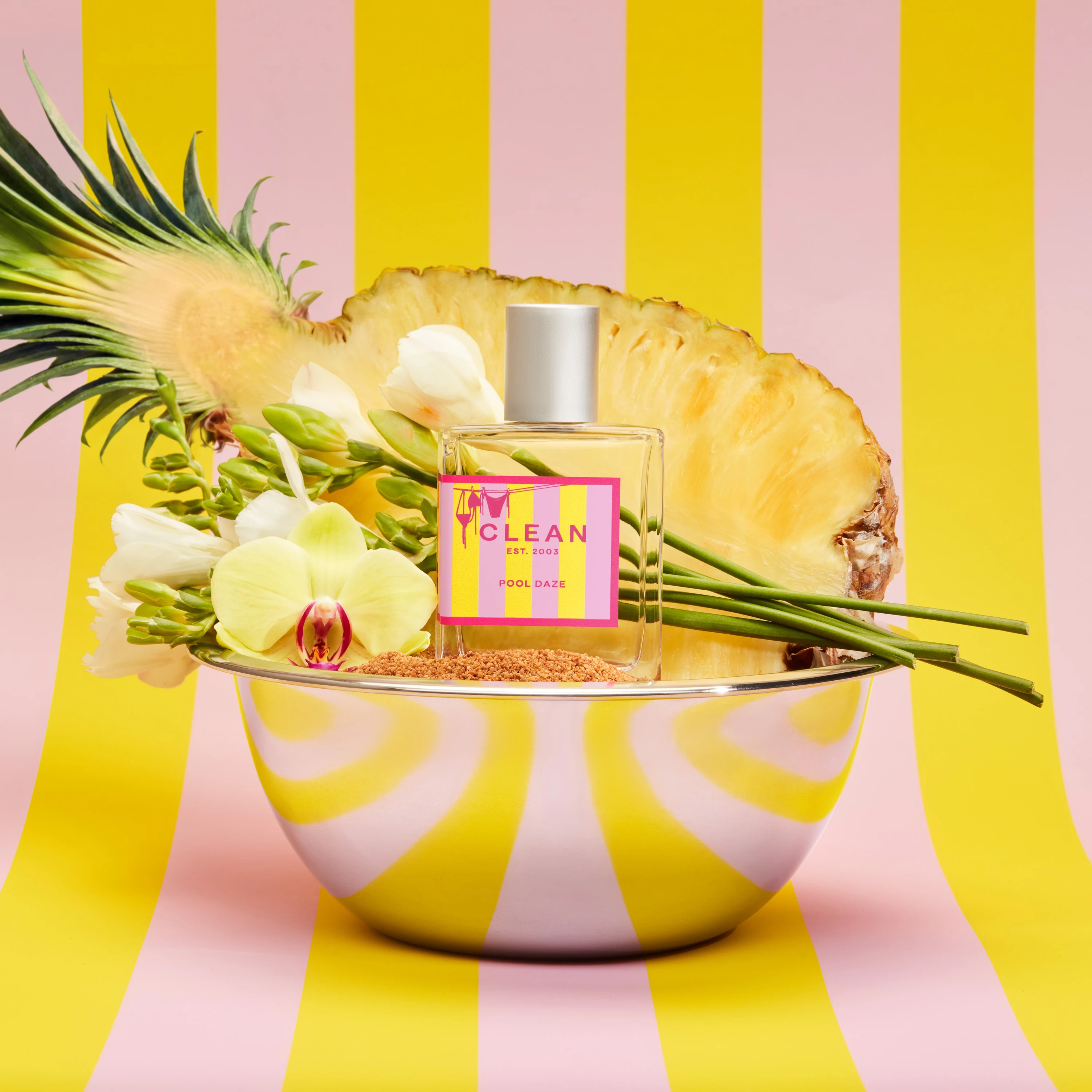 A Clean fragrance bottle with pineapple slices against yellow-and-pink stripes.
