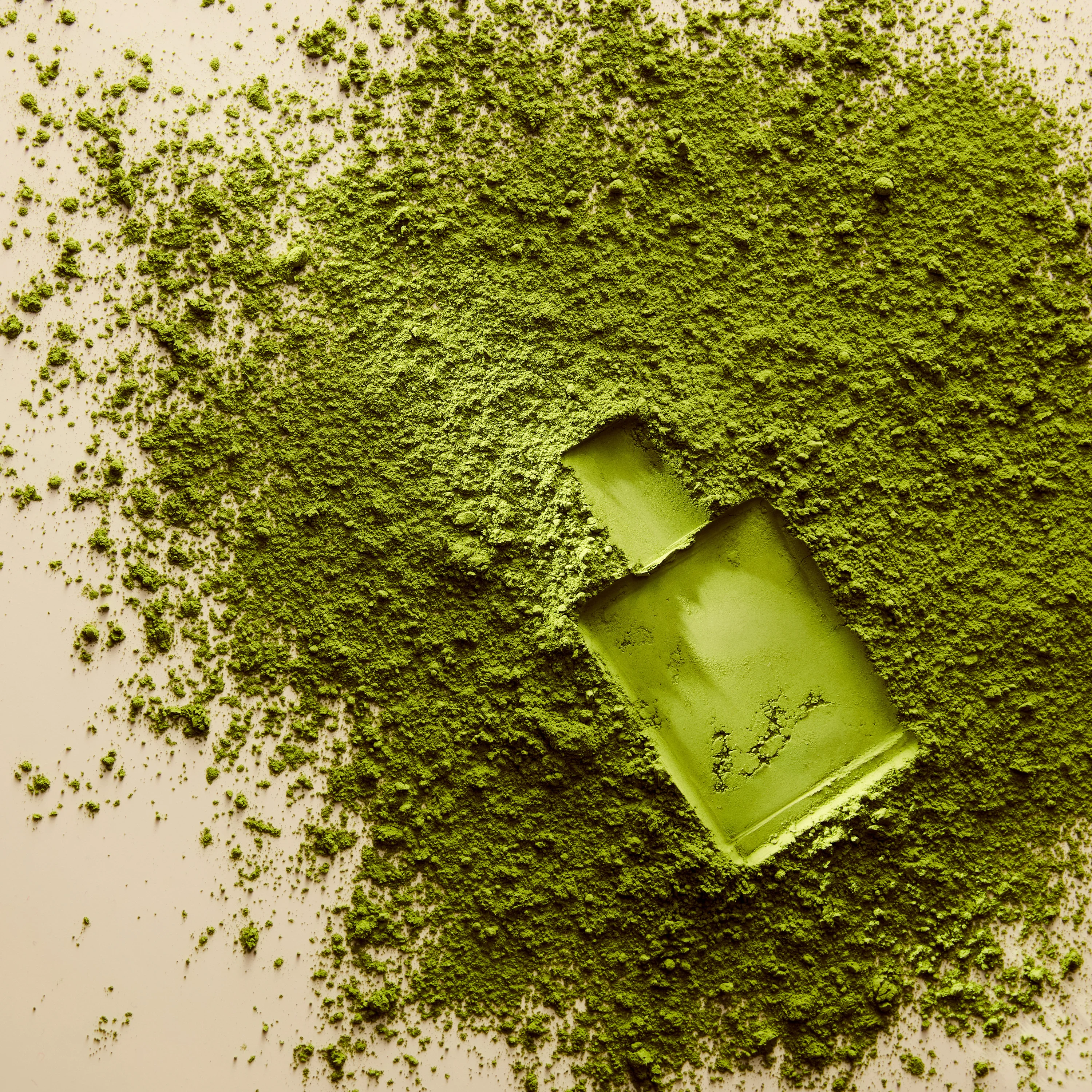 A green Clean fragrance bottle nestled in green powder.
