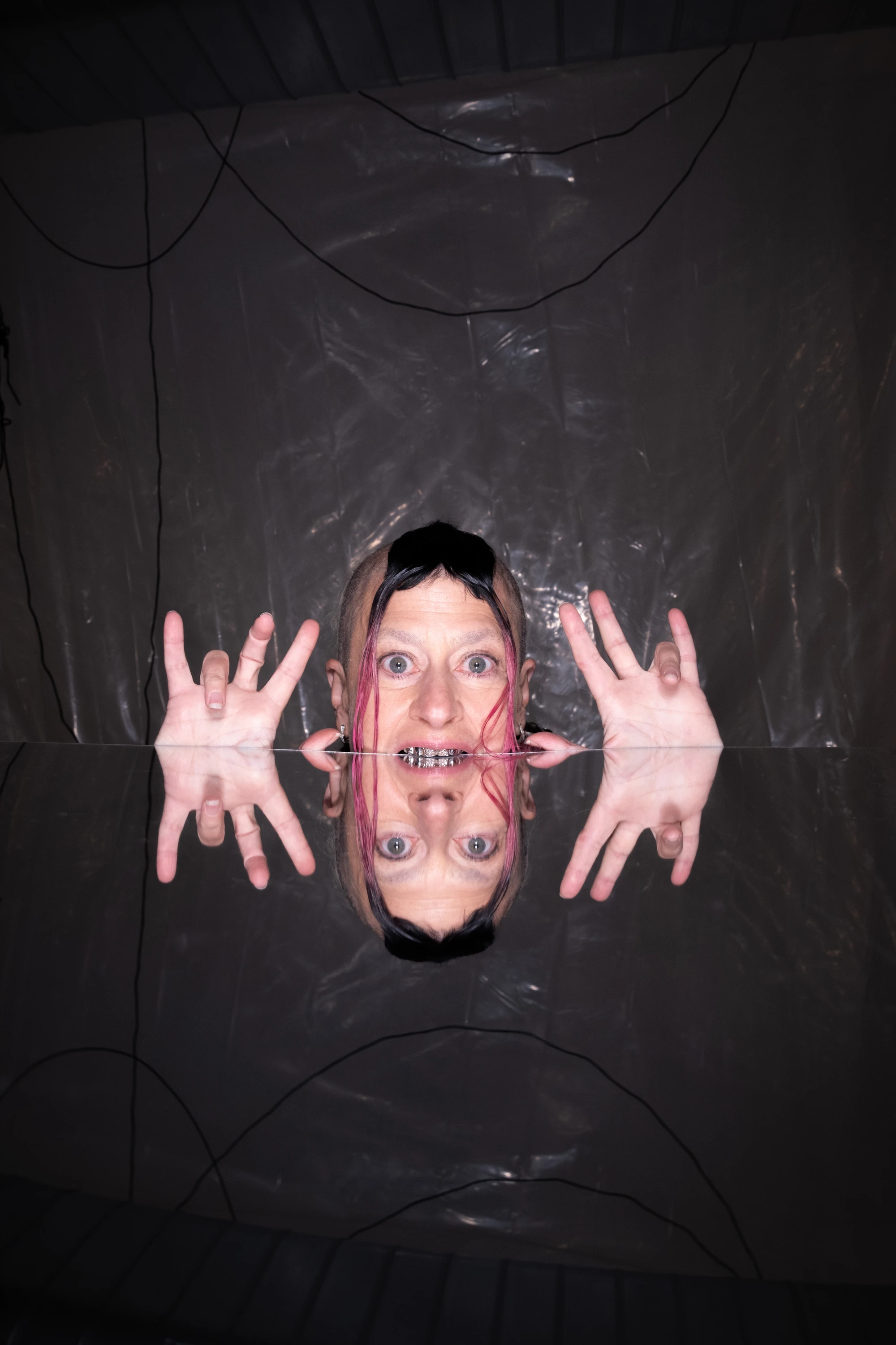 Peaches posing through a dark fabric opening with both hands raised.