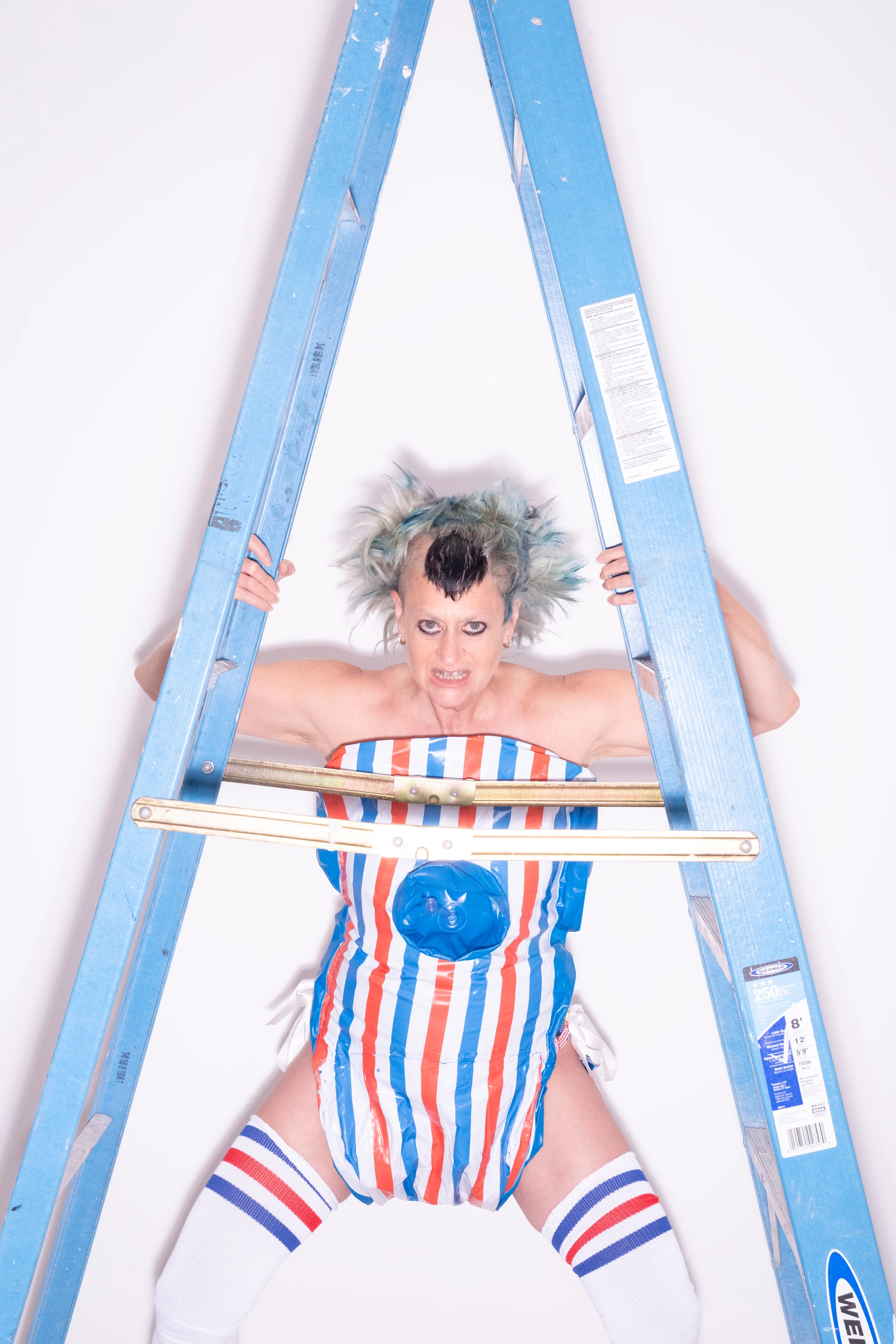 Peaches posing behind a blue ladder in a striped outfit.