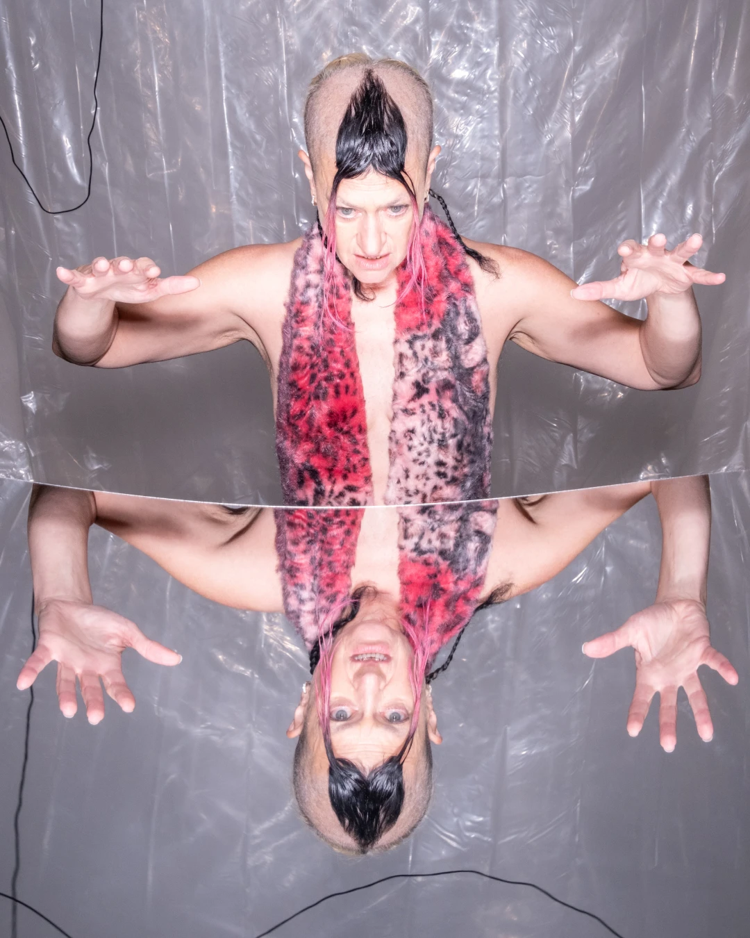 A mirrored editorial portrait of Peaches with arms extended.