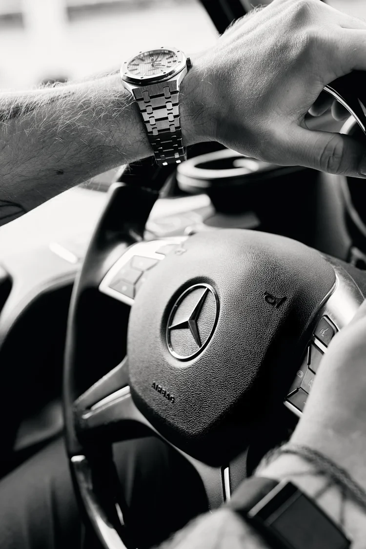 Close-up of a watch and hands on a Mercedes-Benz steering wheel.
