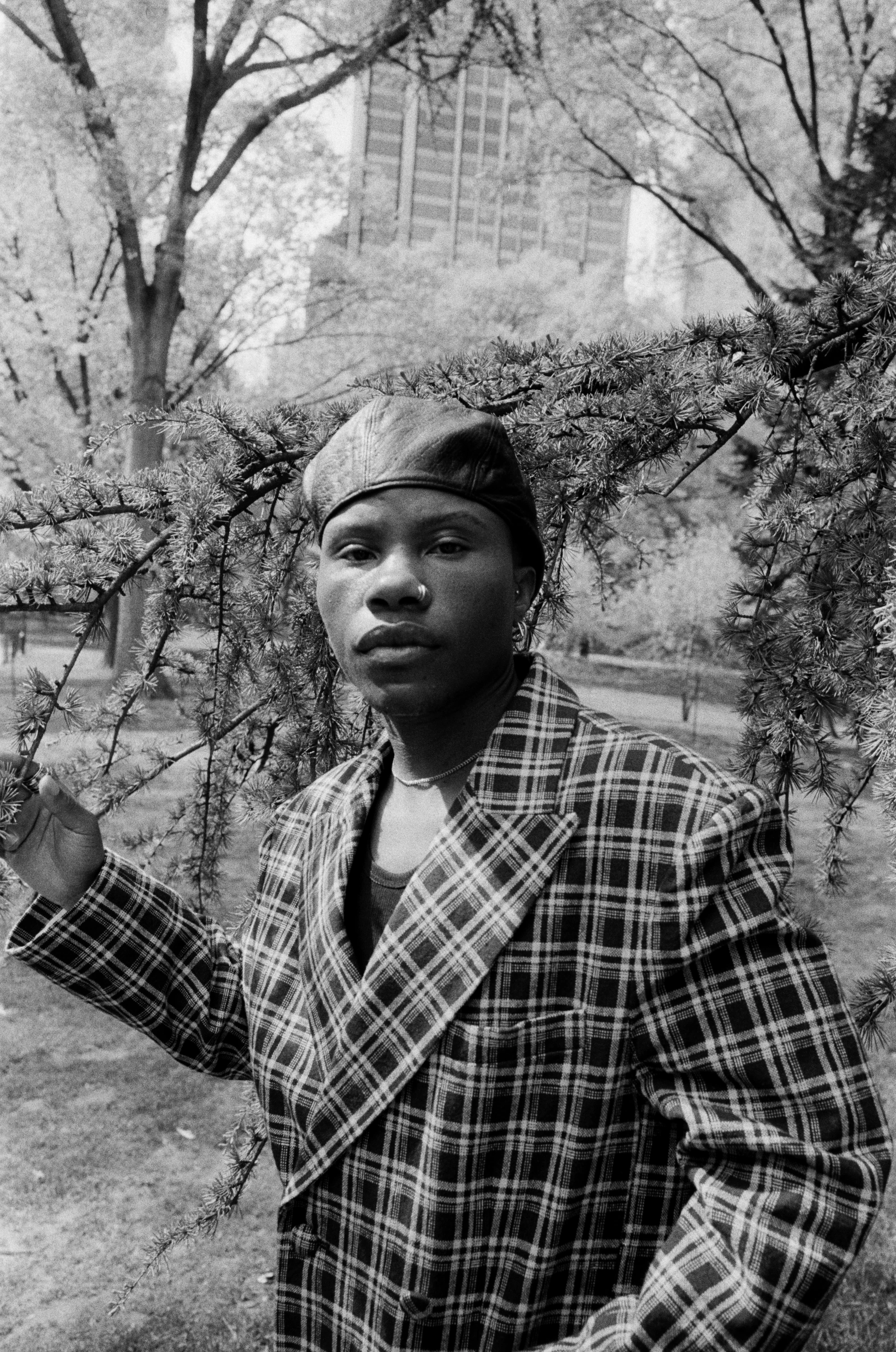 TYGAPAW posing beside a tree in a plaid jacket.