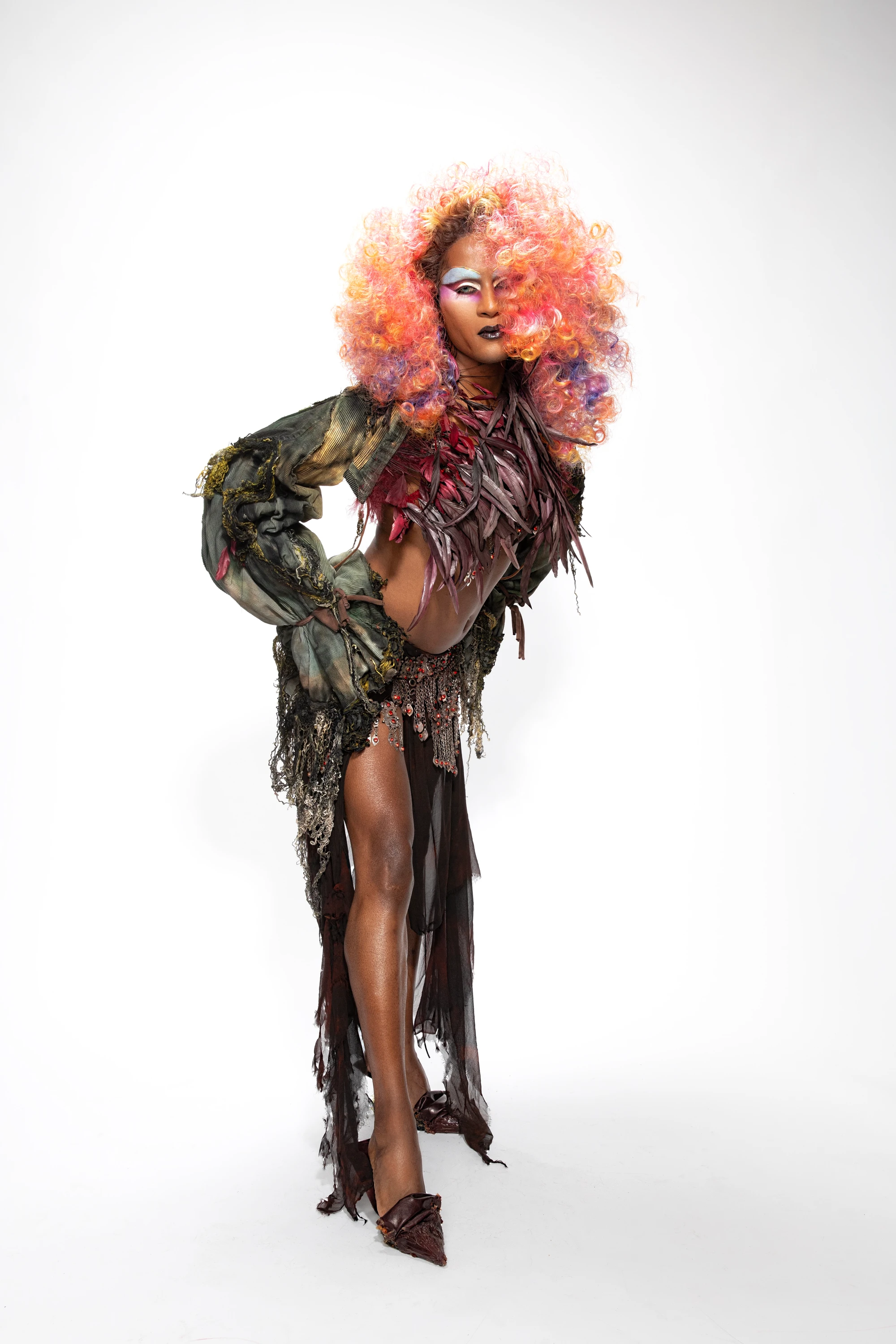 Richie Shazam standing in a dark outfit with pink-orange hair.