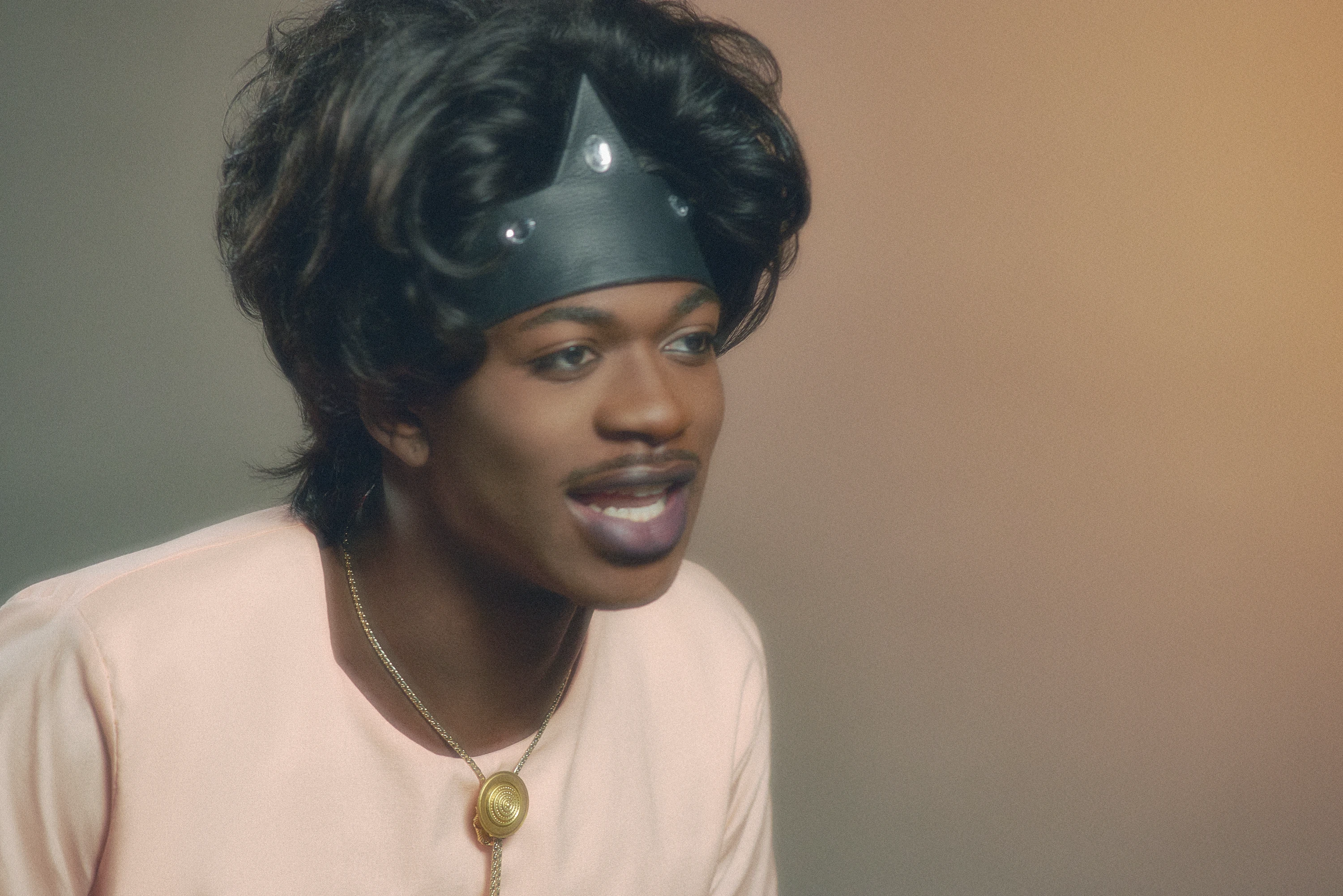 Lil Nas X smiling in a pink shirt and styled hair.