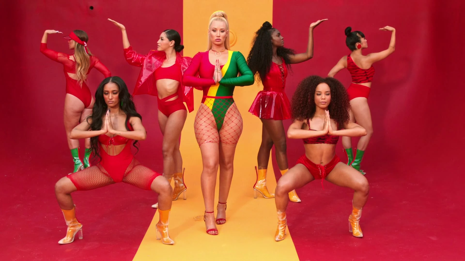 Iggy Azalea performing with dancers on a red-and-yellow set.