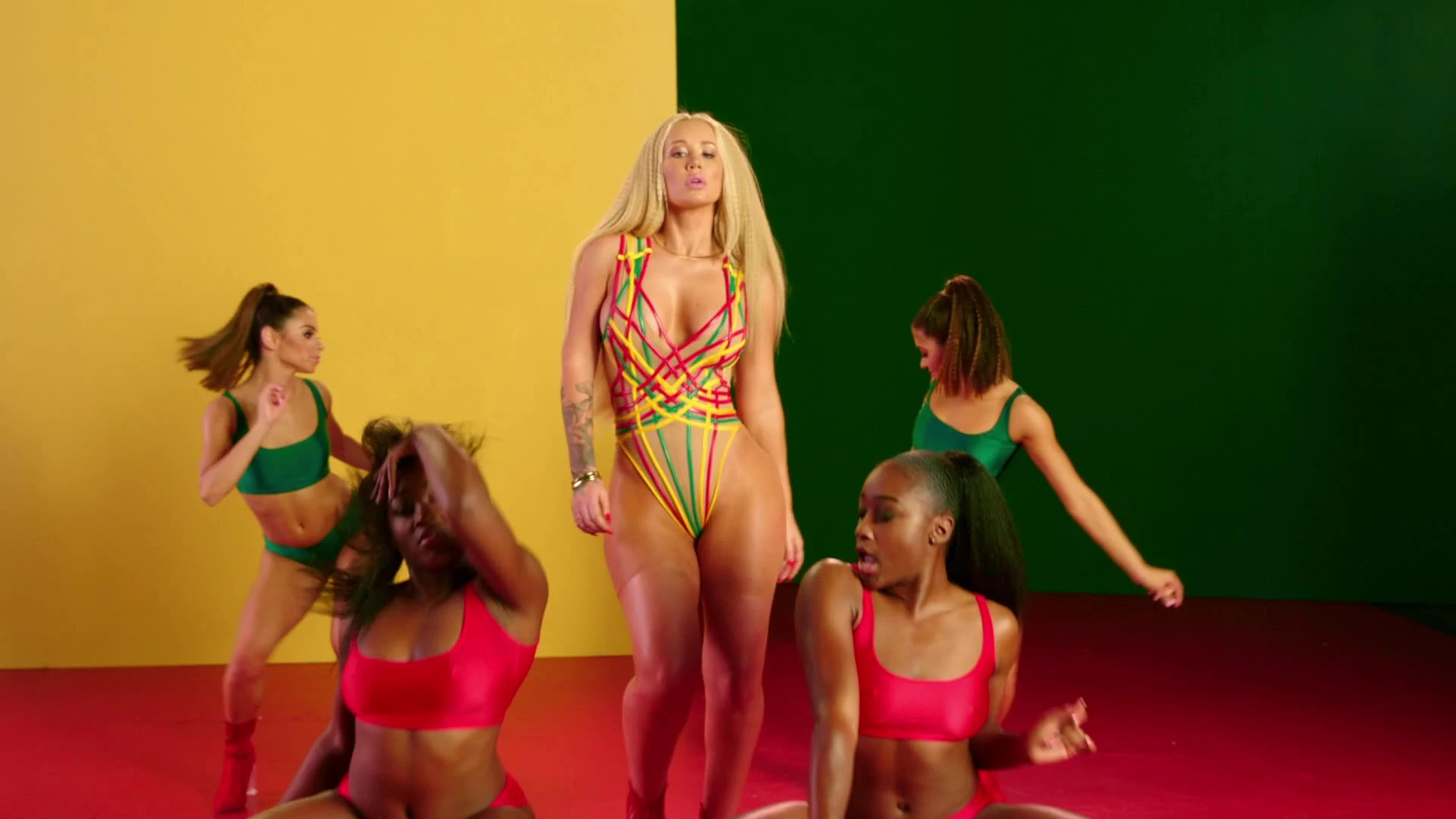 Iggy Azalea and dancers against a yellow-and-green backdrop.