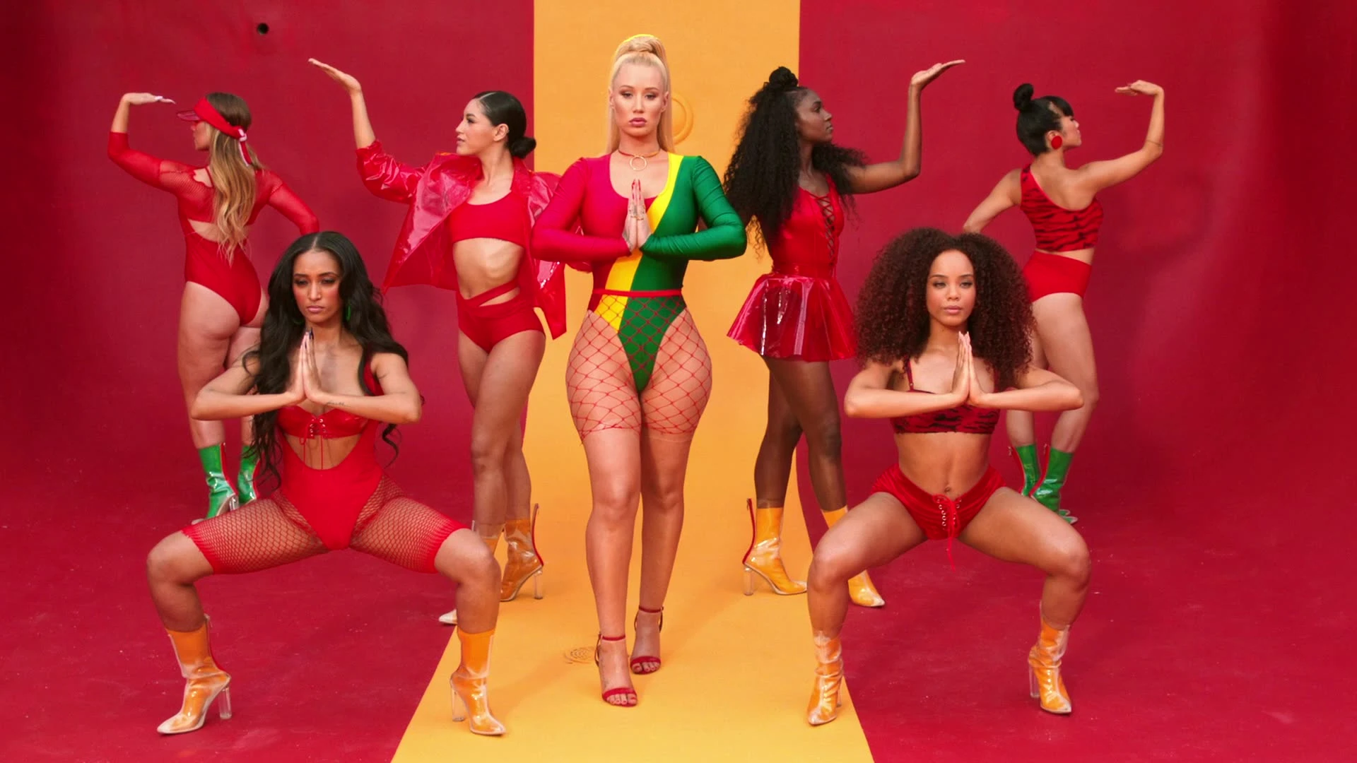 Iggy Azalea and dancers posing on a red-and-yellow set.