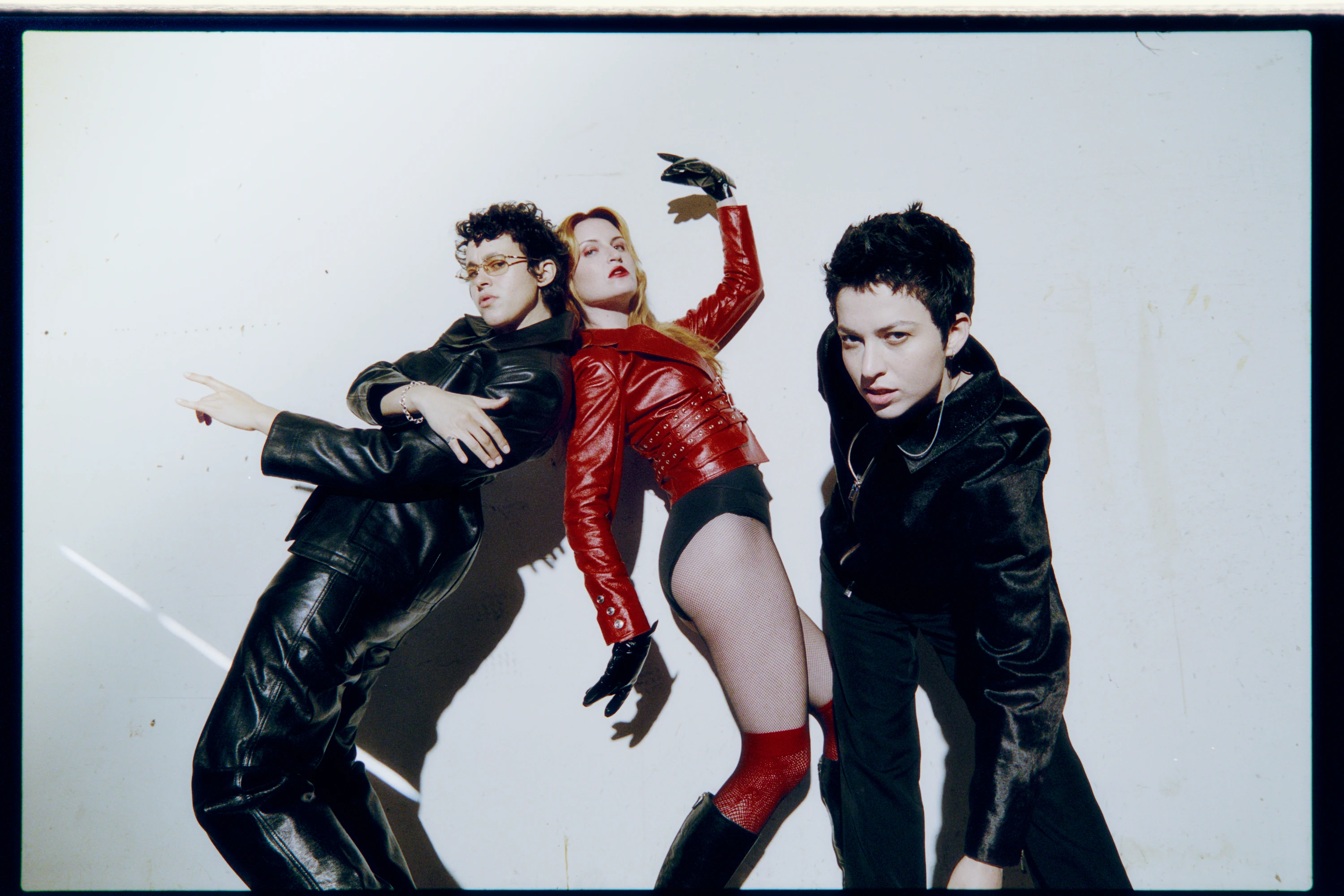 MUNA posing in black and red outfits against a pale backdrop.