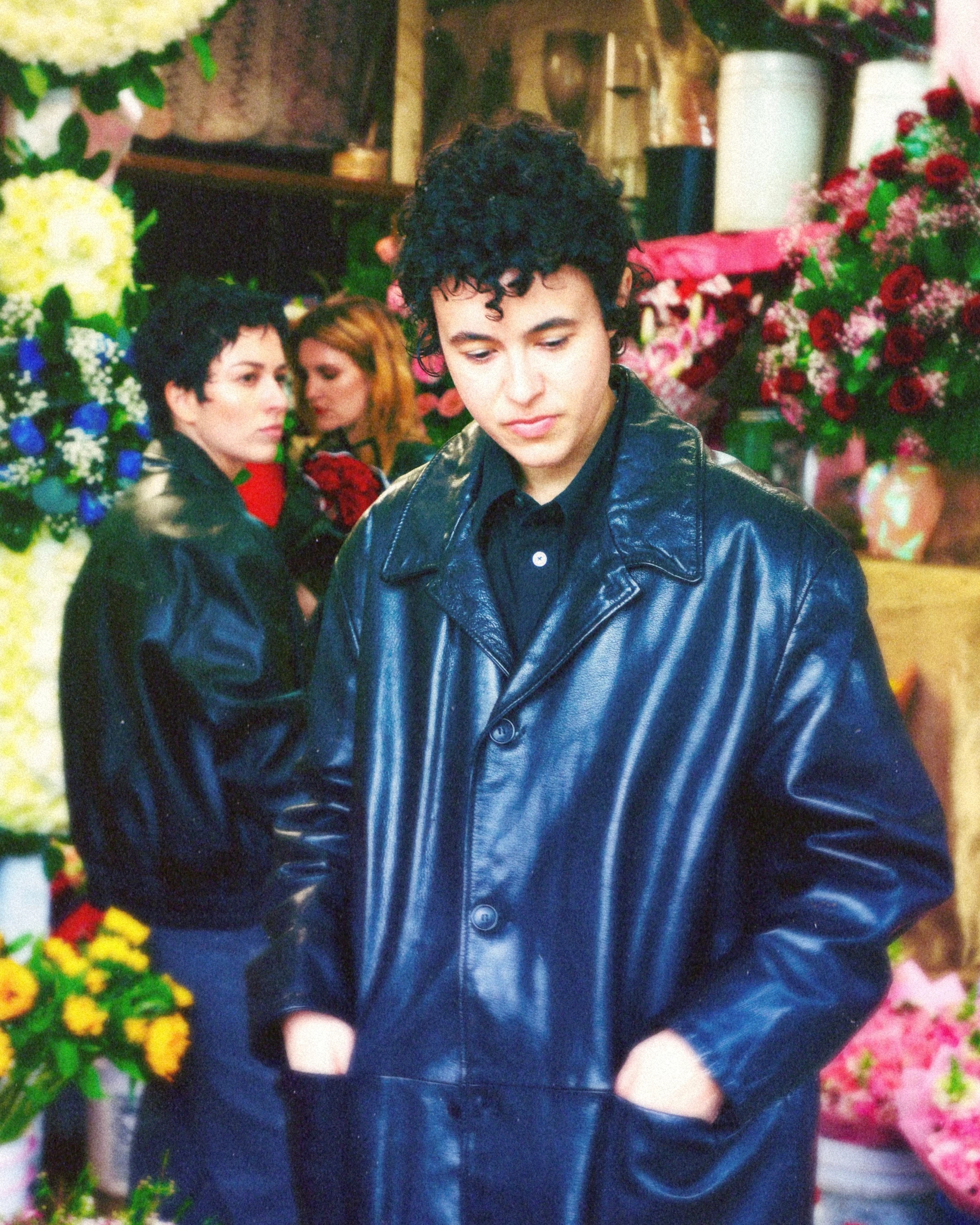 MUNA posing in black jackets beside colorful flowers.
