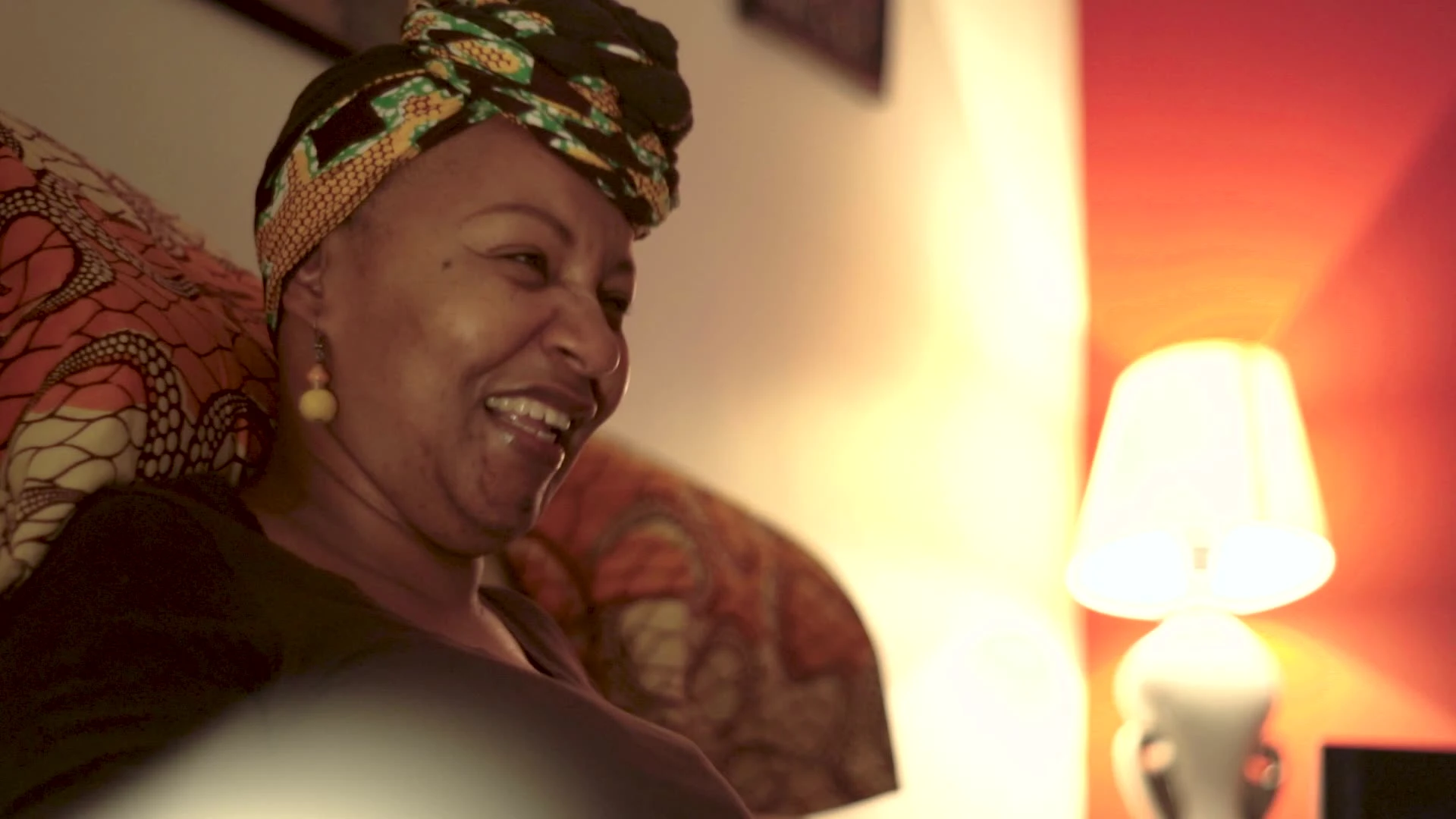 A person laughing indoors beside a lit lamp.