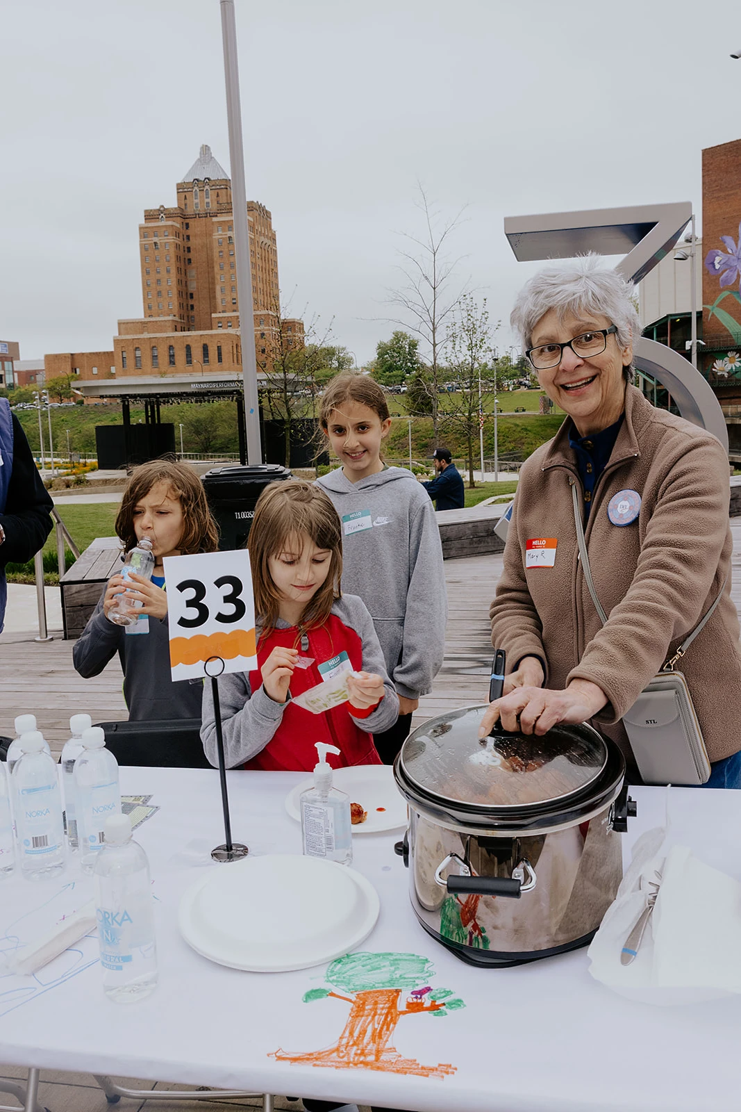 A participant serving food at a numbered outdoor table.