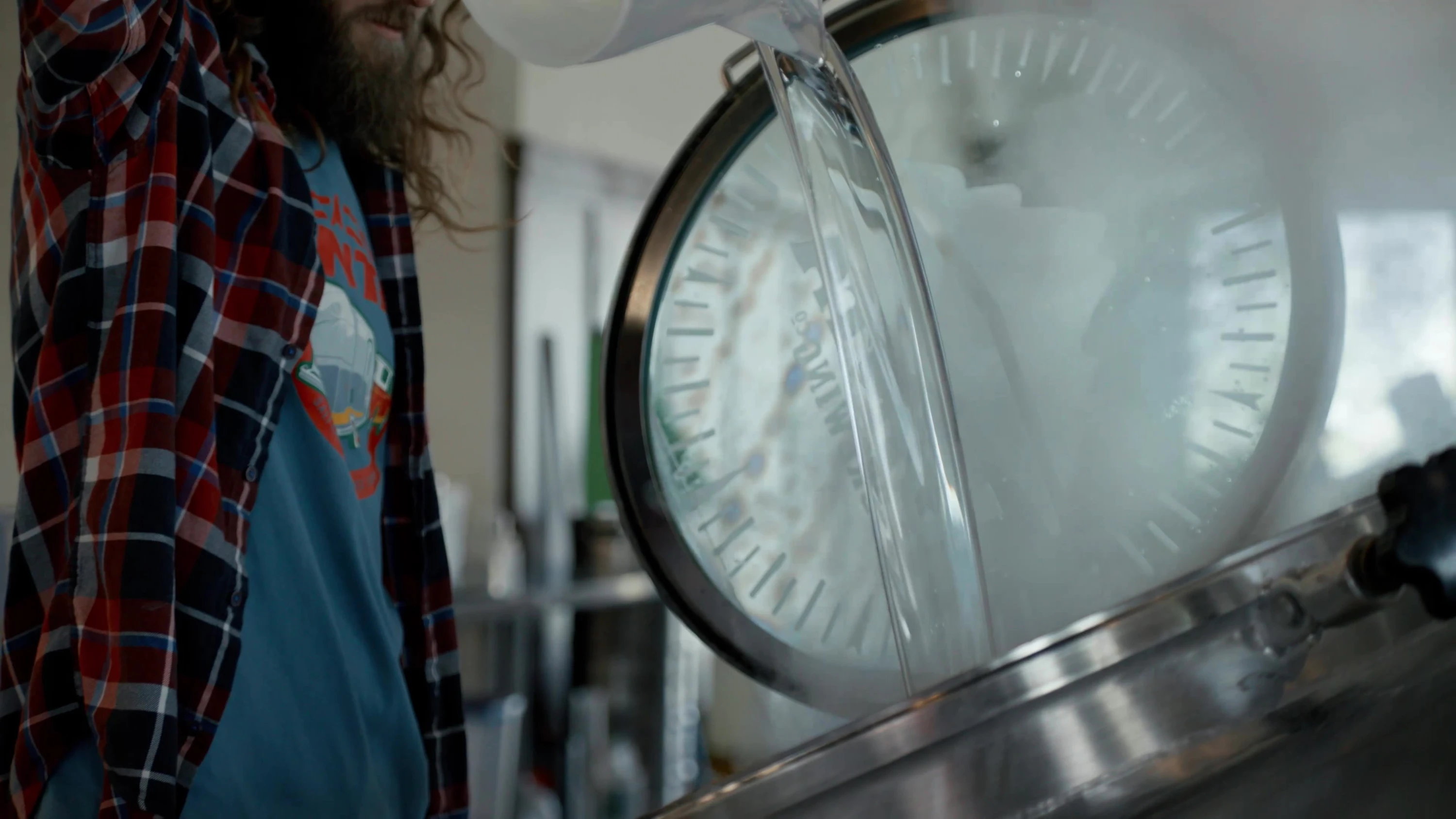 A worker lifting the lid of a brewing vessel.