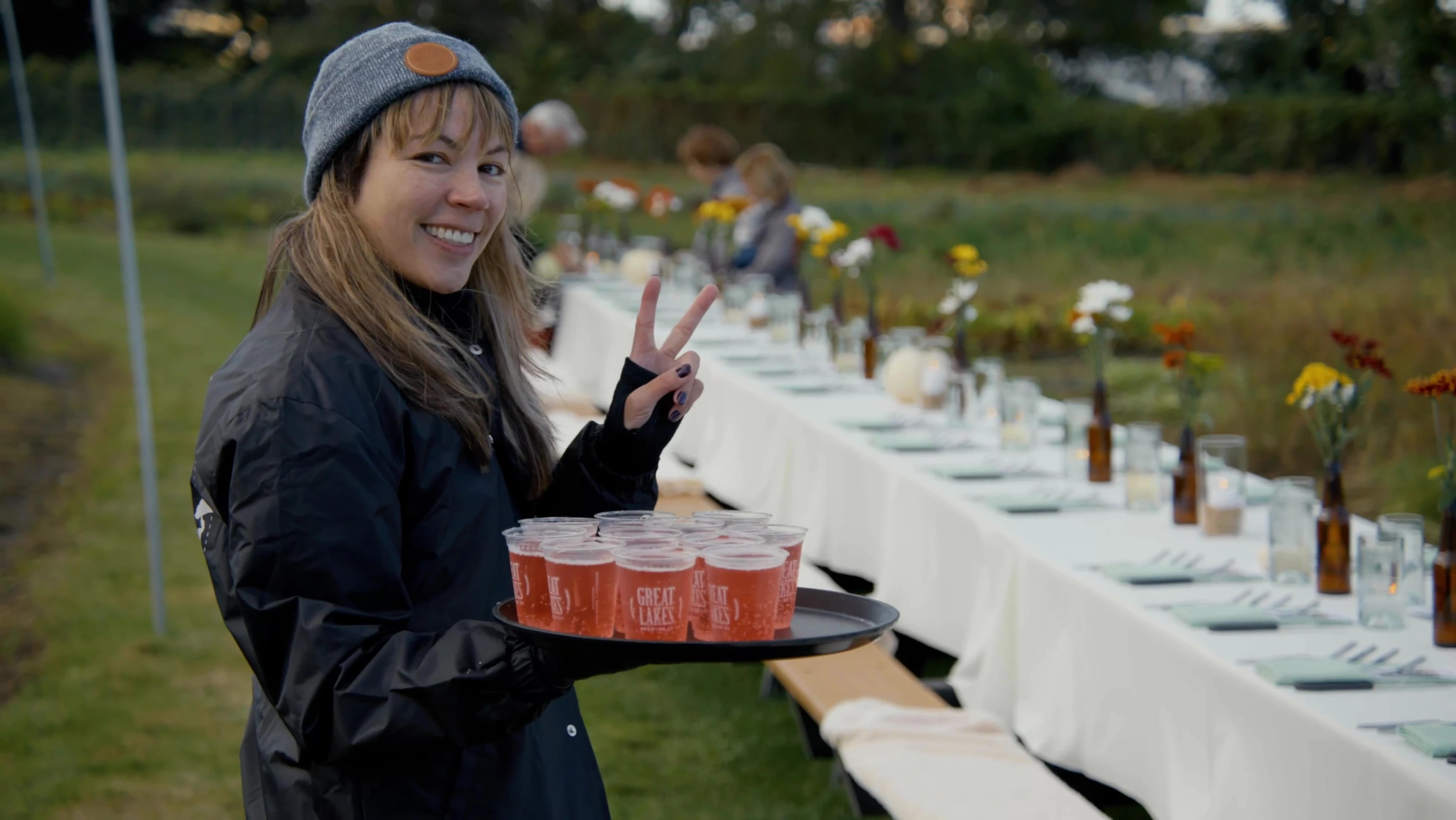 A server carrying drinks beside a long outdoor table.
