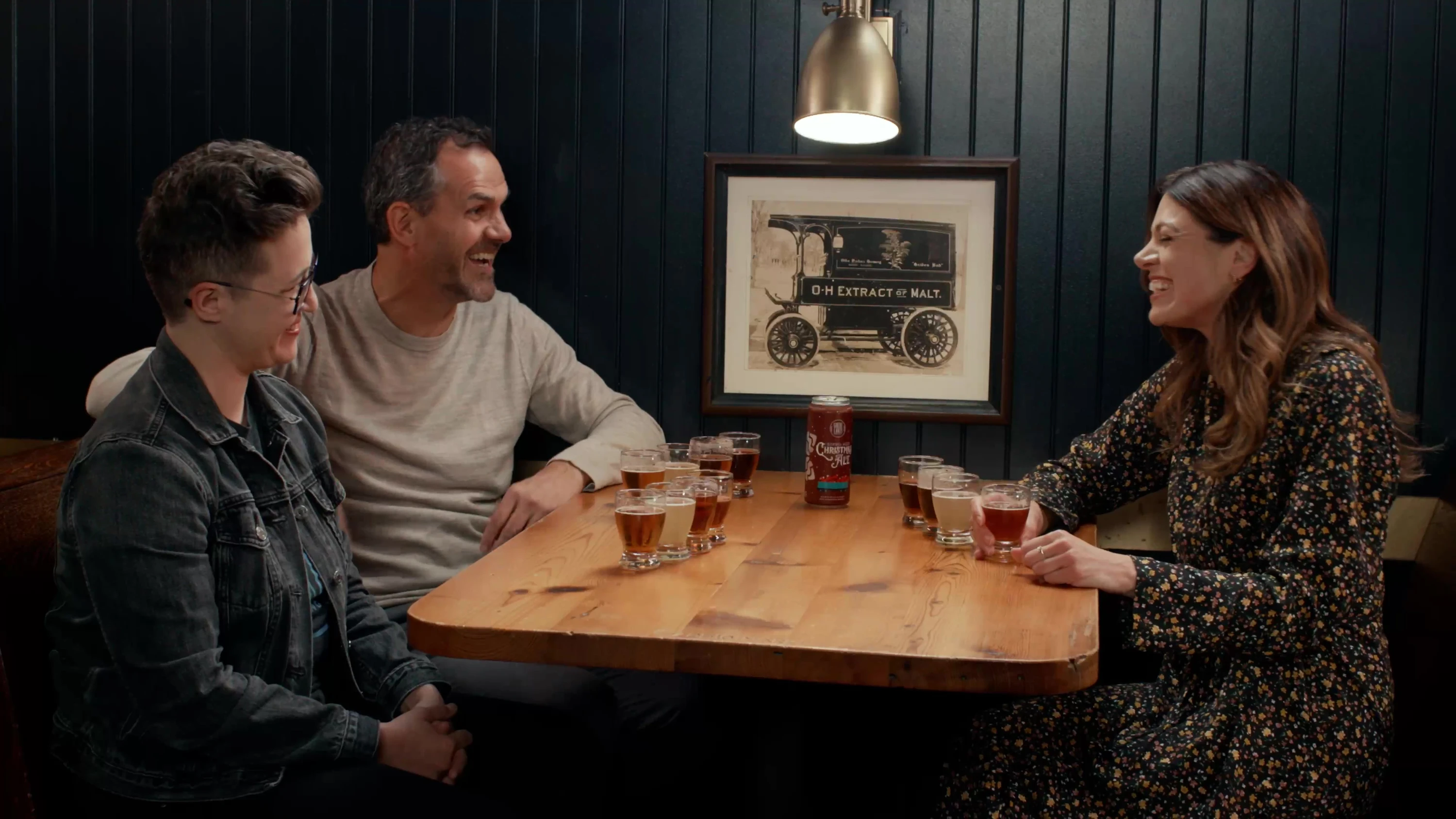 Three people talking around a wooden table with tasting glasses.
