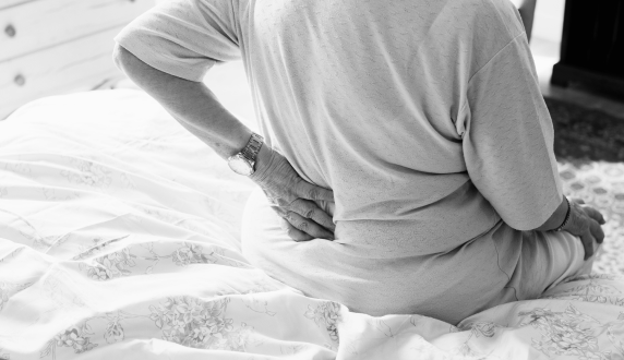 Person sitting on a bed holding their lower back