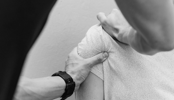 A clinician assessing a patient's shoulder with both hands