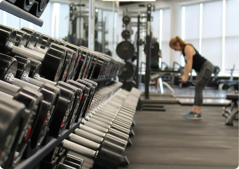 A gym with a rack of dumbbells and a person training in the background