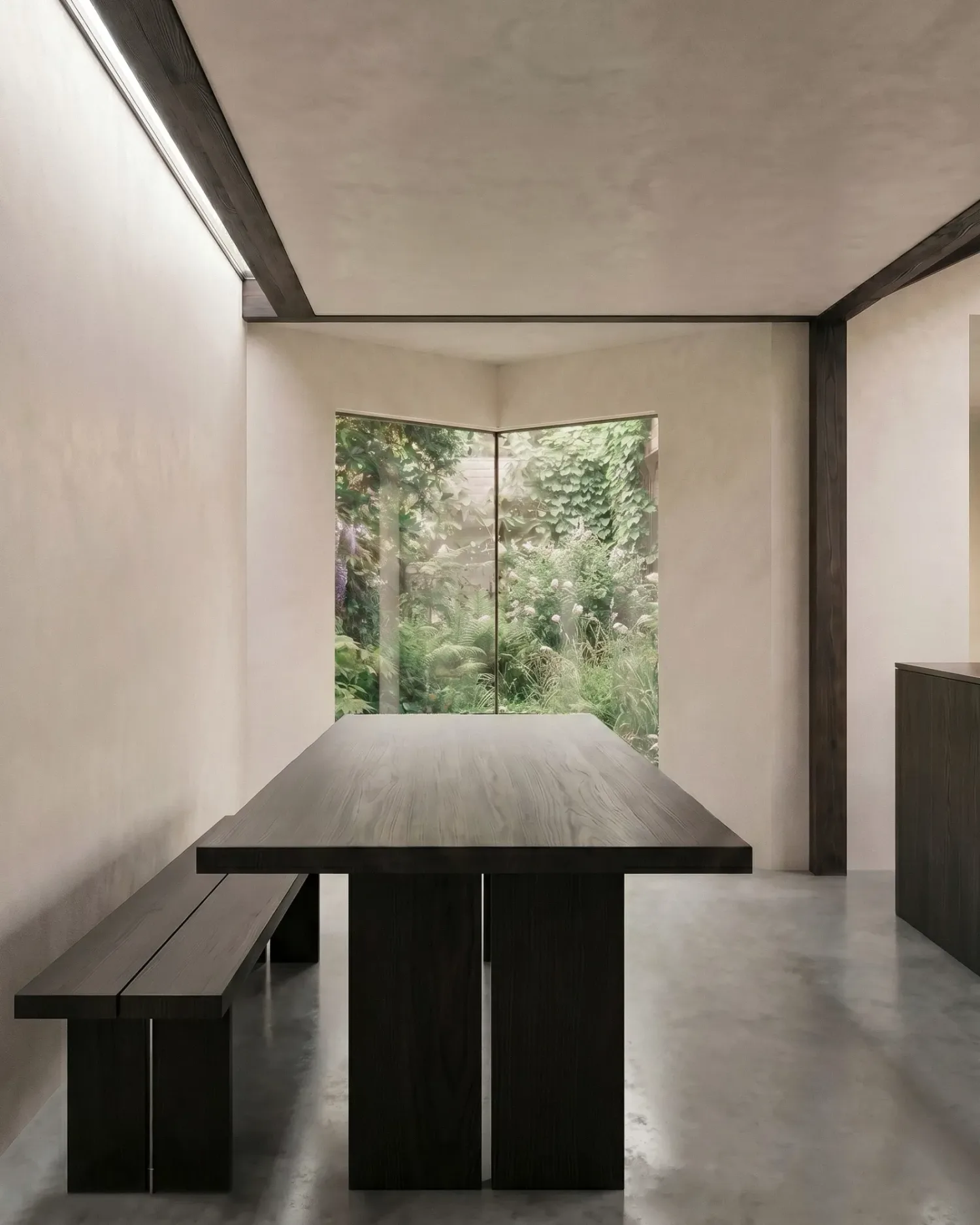 The dining table lit by a narrow slot rooflight overhead, with the chamfered corner window framing the garden beyond