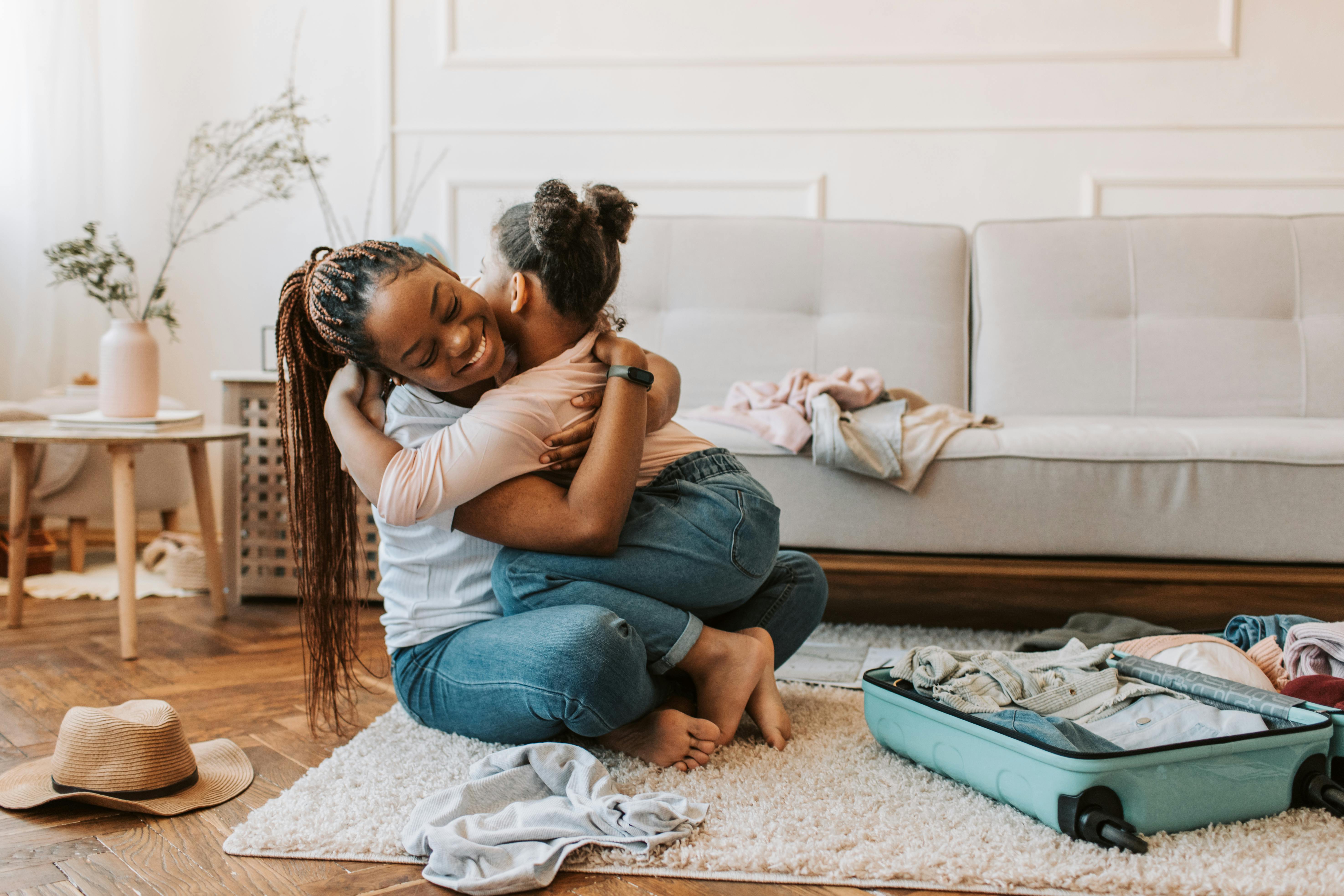 Mom and daughter hugging next to sofa and open suitcase with clothes stock image
