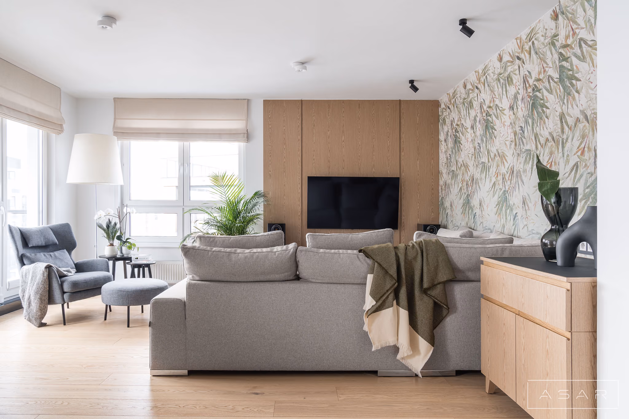 Salon z jasną sofą, drewnianą zabudową i dekoracyjną tapetą w Apartamencie Oliwa – ASAR PROJEKT