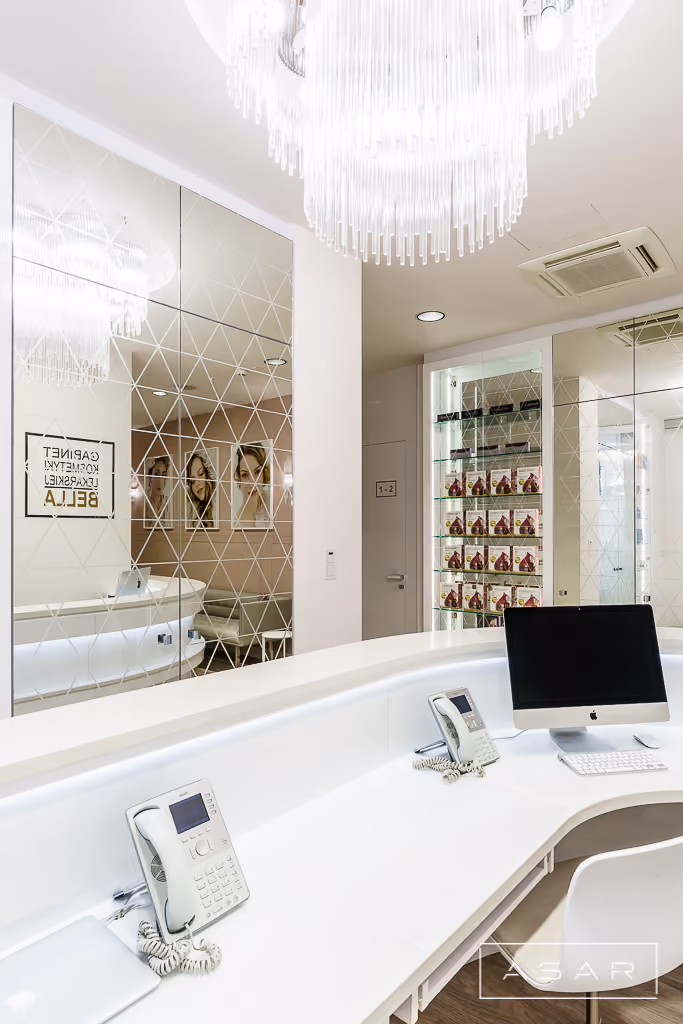 Strefa recepcji Kliniki Bella z jasnym biurkiem, dekoracyjnymi grafikami i eleganckim oświetleniem – ASAR Projekt