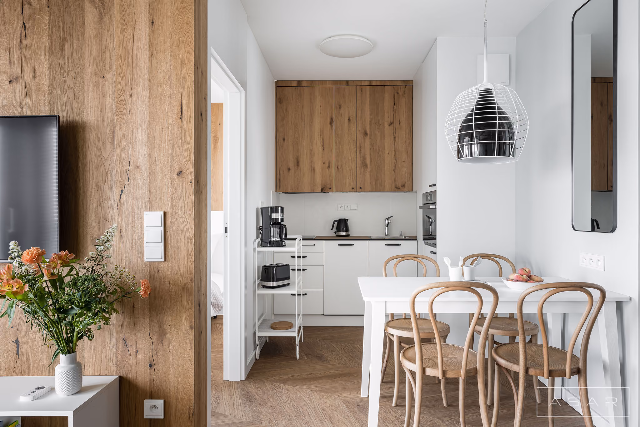 Kuchnia i jadalnia apartamentu nad morzem z drewnianą zabudową i jasnymi meblami – ASAR Projekt