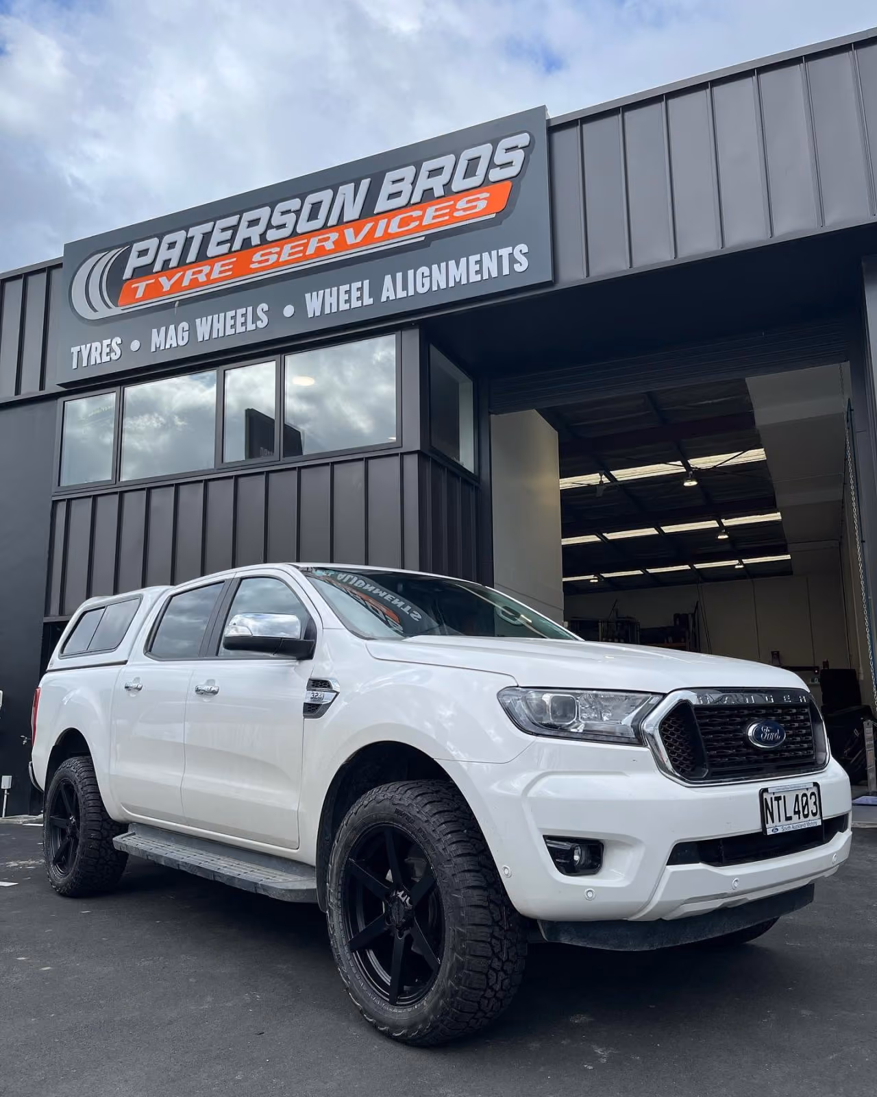 White Ford pickup truck with black wheels parked outside Paterson Bros Tyre Services garage.