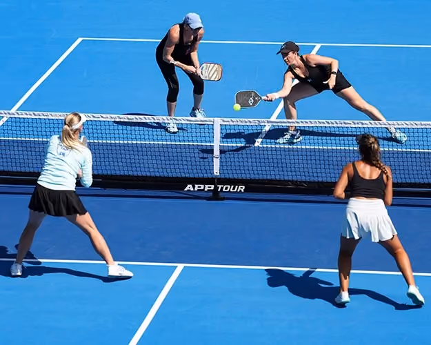 Four players mid-rally in a doubles pickleball match on a blue APP Tour court