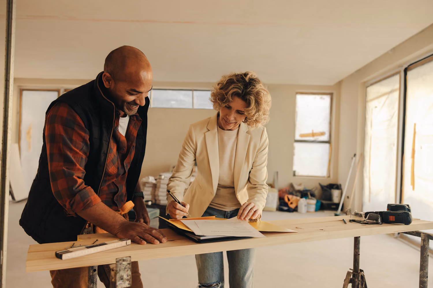 Two people, a man and a woman, reviewing documents on a table in a room under renovation.