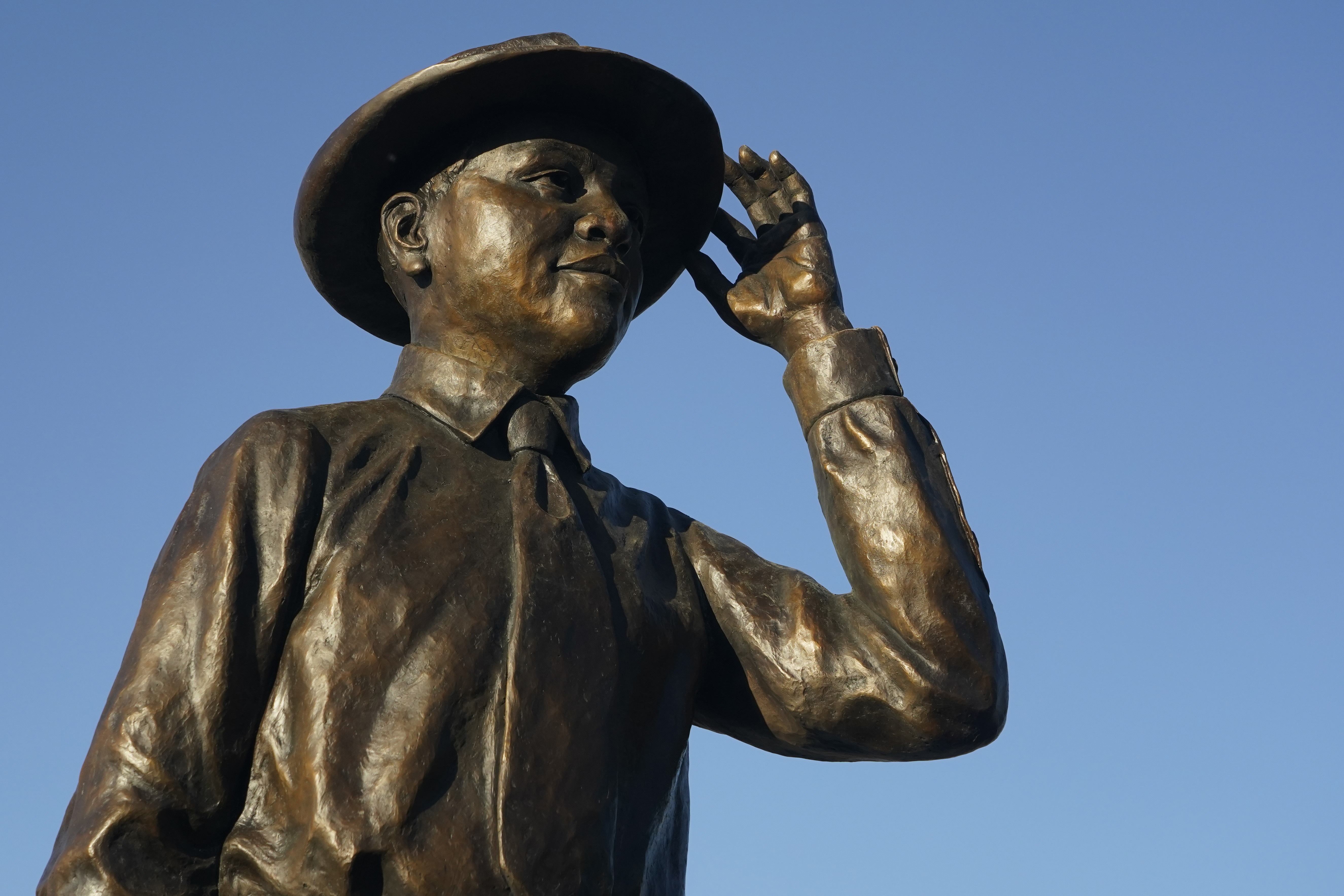 A bronze statue of Emmett Till stands against a blue sky.