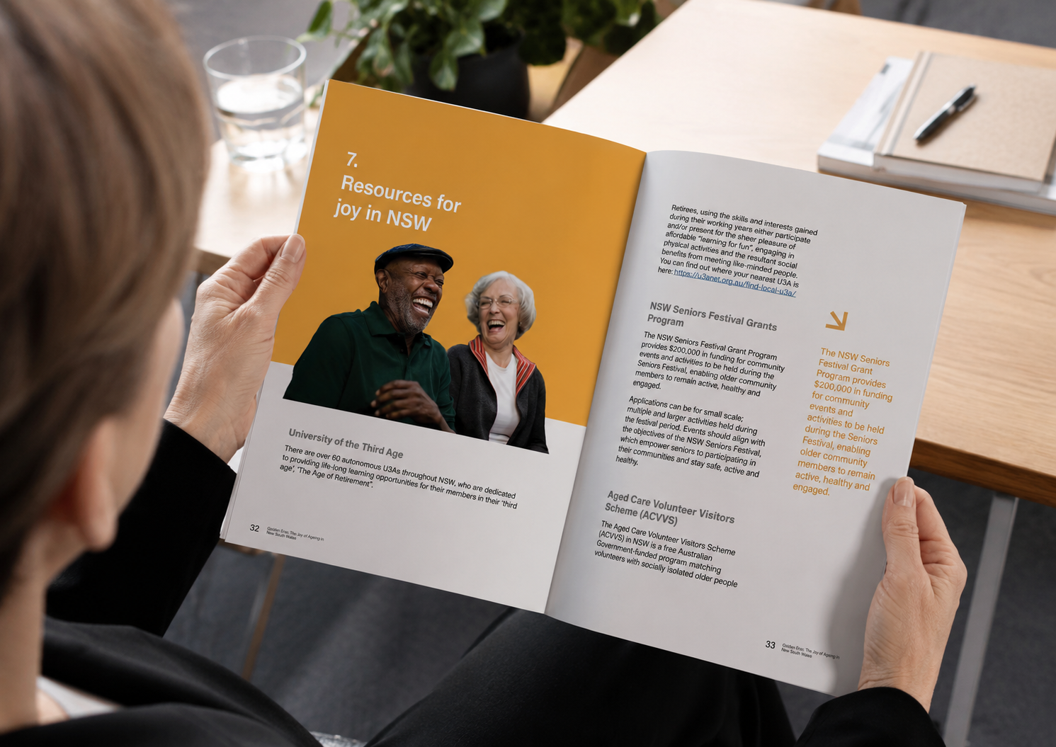 Person holding open a booklet titled '7. Resources for joy in NSW' featuring a photo of a laughing older man and woman, with text about University of the Third Age, NSW Seniors Festival Grants, and Aged Care Volunteer Visitors Scheme.
