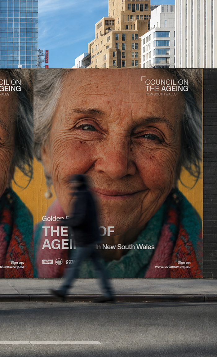 Large billboard on a city street featuring a close-up portrait of an elderly woman with a gentle smile, promoting the Council on the Ageing New South Wales with text about ageing in New South Wales, while a blurred person walks past in front of it.