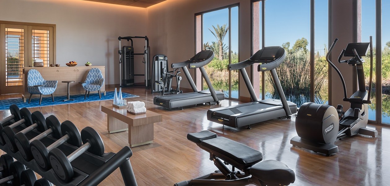 Salle de fitness avec appareils et vue sur la végétation. The Oberoi, Marrakech, Marrakech.